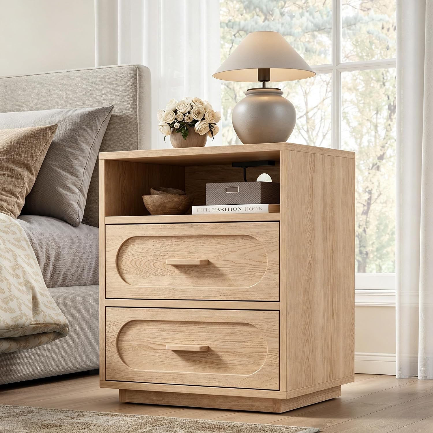 Light oak two-drawer nightstand with open top shelf holding a lamp, vase and storage box, charging port visible inside.