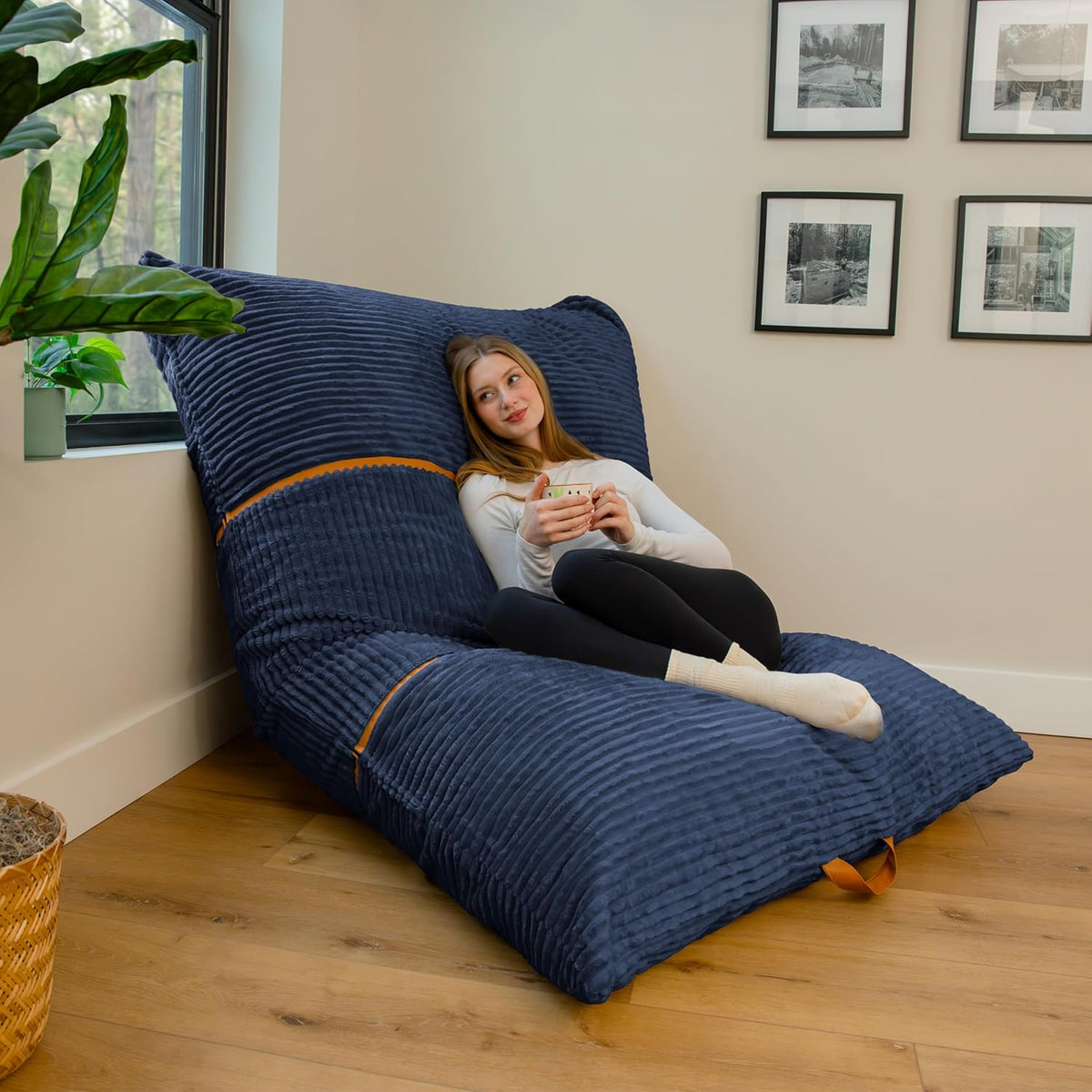 Side view of a tall navy ribbed lounger beside a window and plant, a woman reclining while holding a mug.