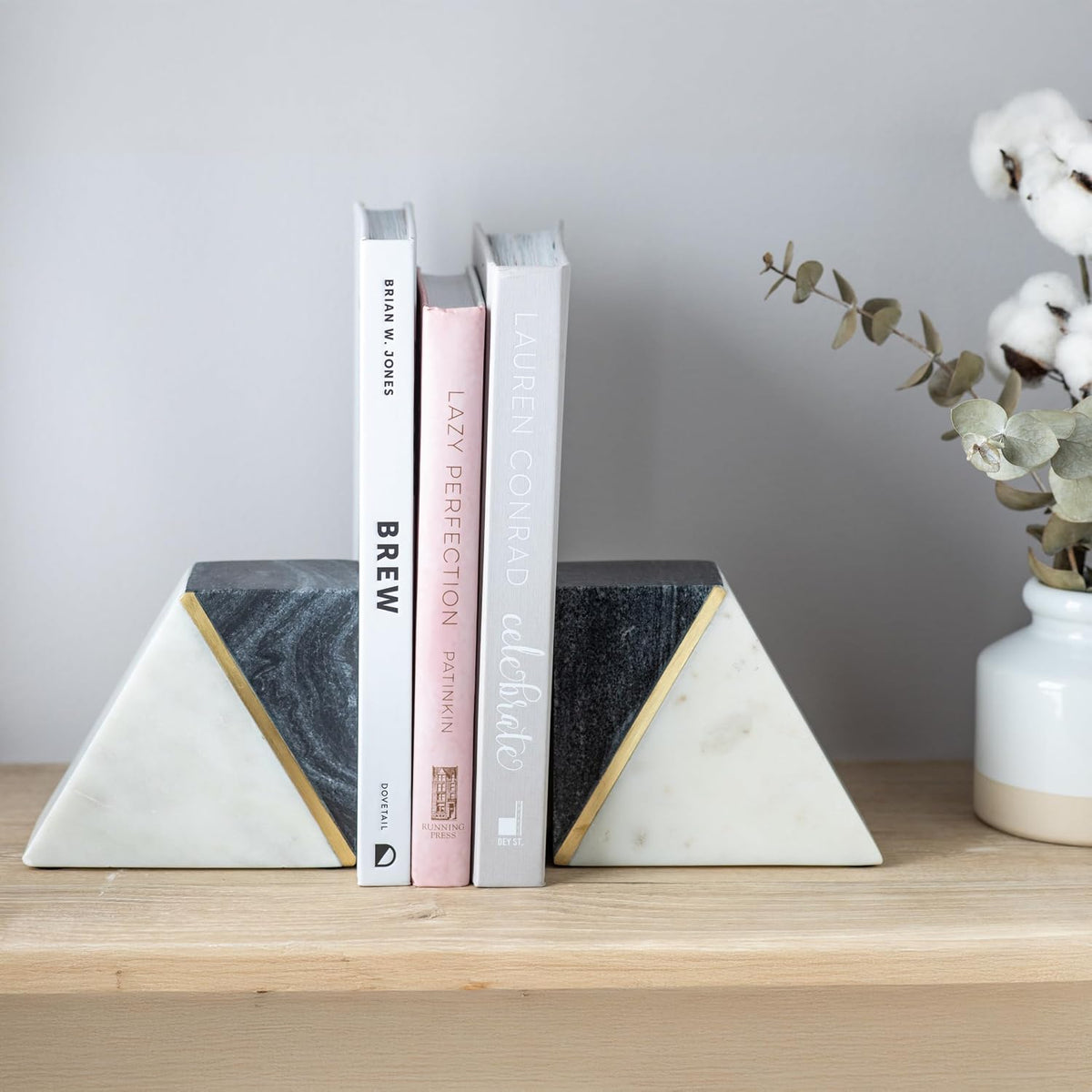 Front view of two triangular marble bookends holding three slim books, with a cotton stem arrangement at right.