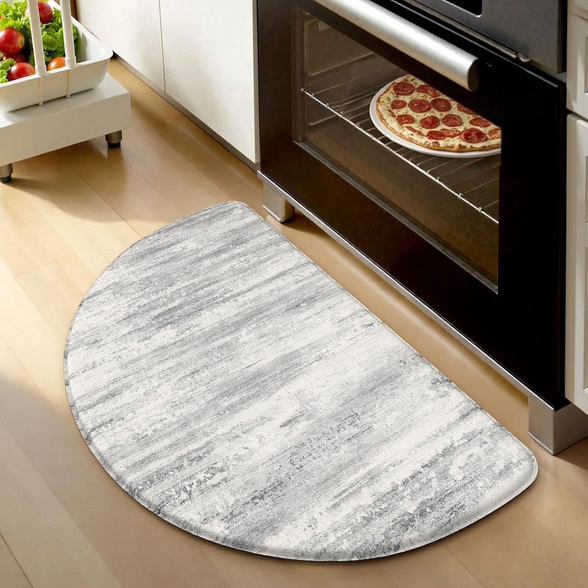 Semi‑oval light-gray kitchen mat placed in front of a black oven, wooden floor and a small white cart visible.