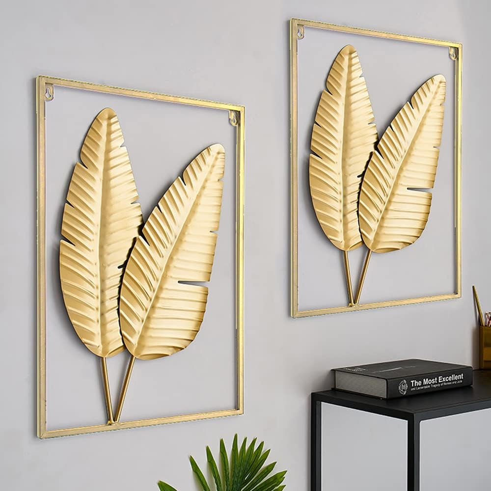 Two gold framed metal leaf wall hangings angled front view on a light grey wall