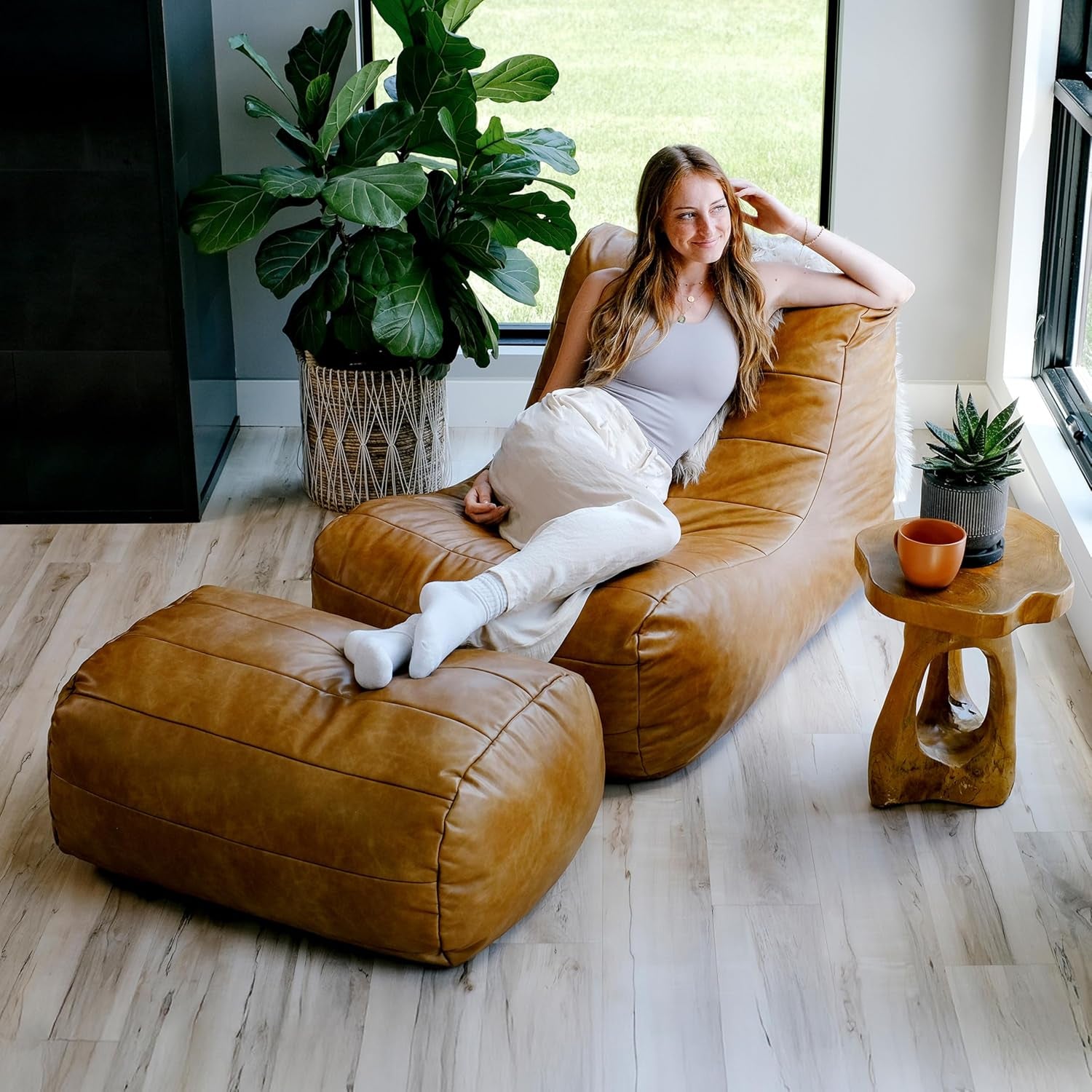 Caramel tan lounge chair and ottoman beside a window and side table, angled overhead with person lounging