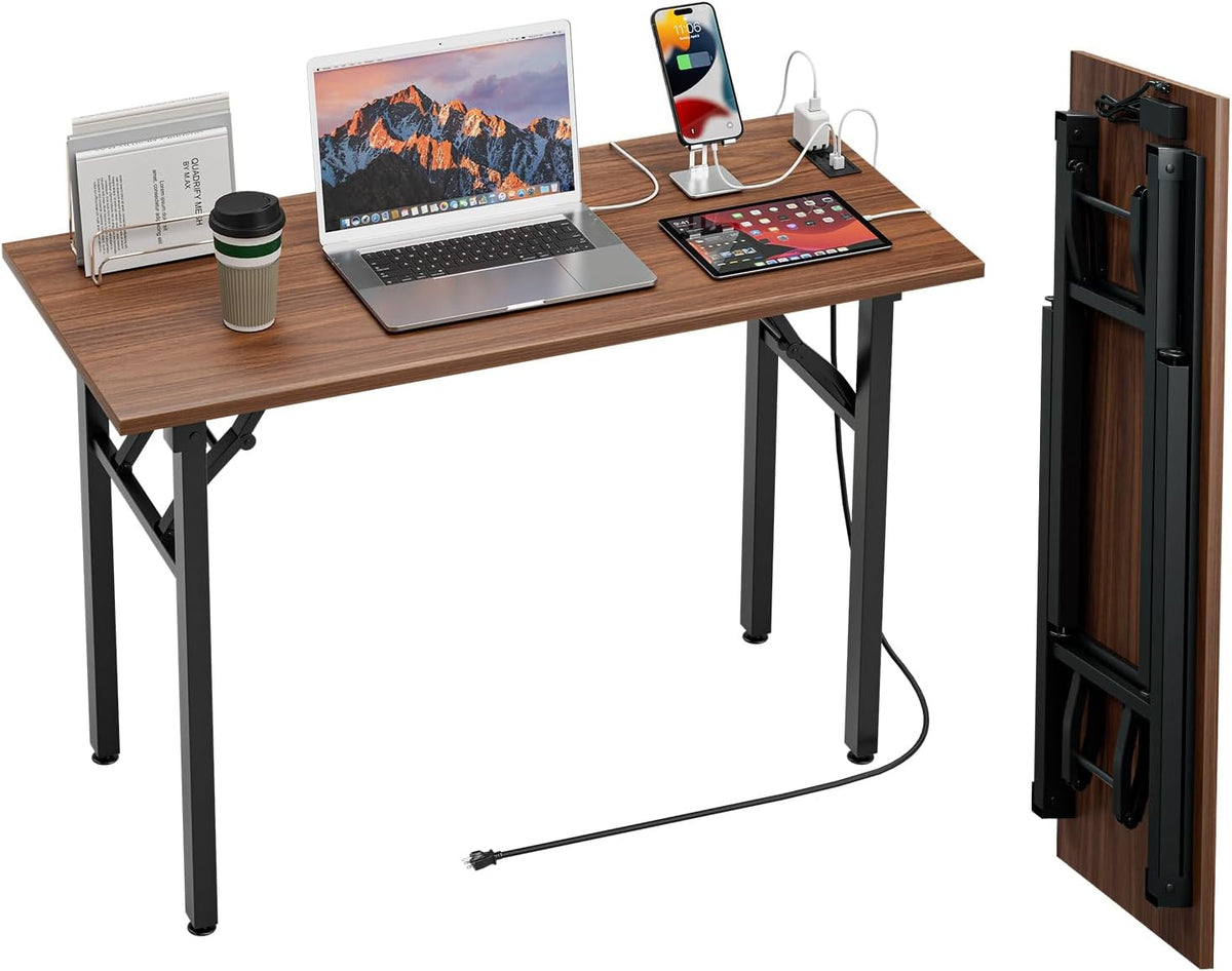 Angled top-down view of the desk loaded with devices and a book rack, power cord trailing from the underside to the plug on