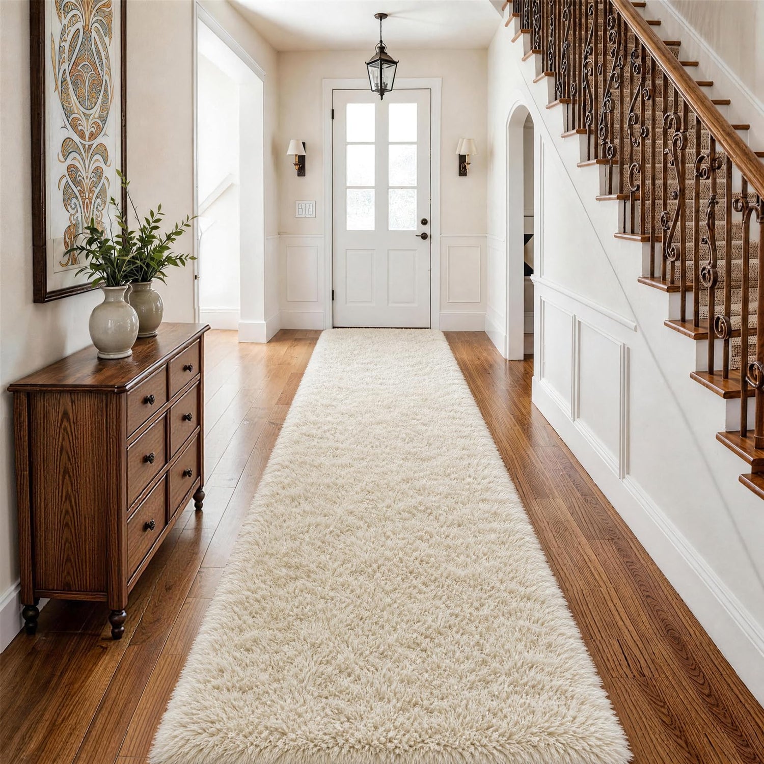 Entryway perspective with cream shag runner down center, wooden chest and decorative staircase on the right.
