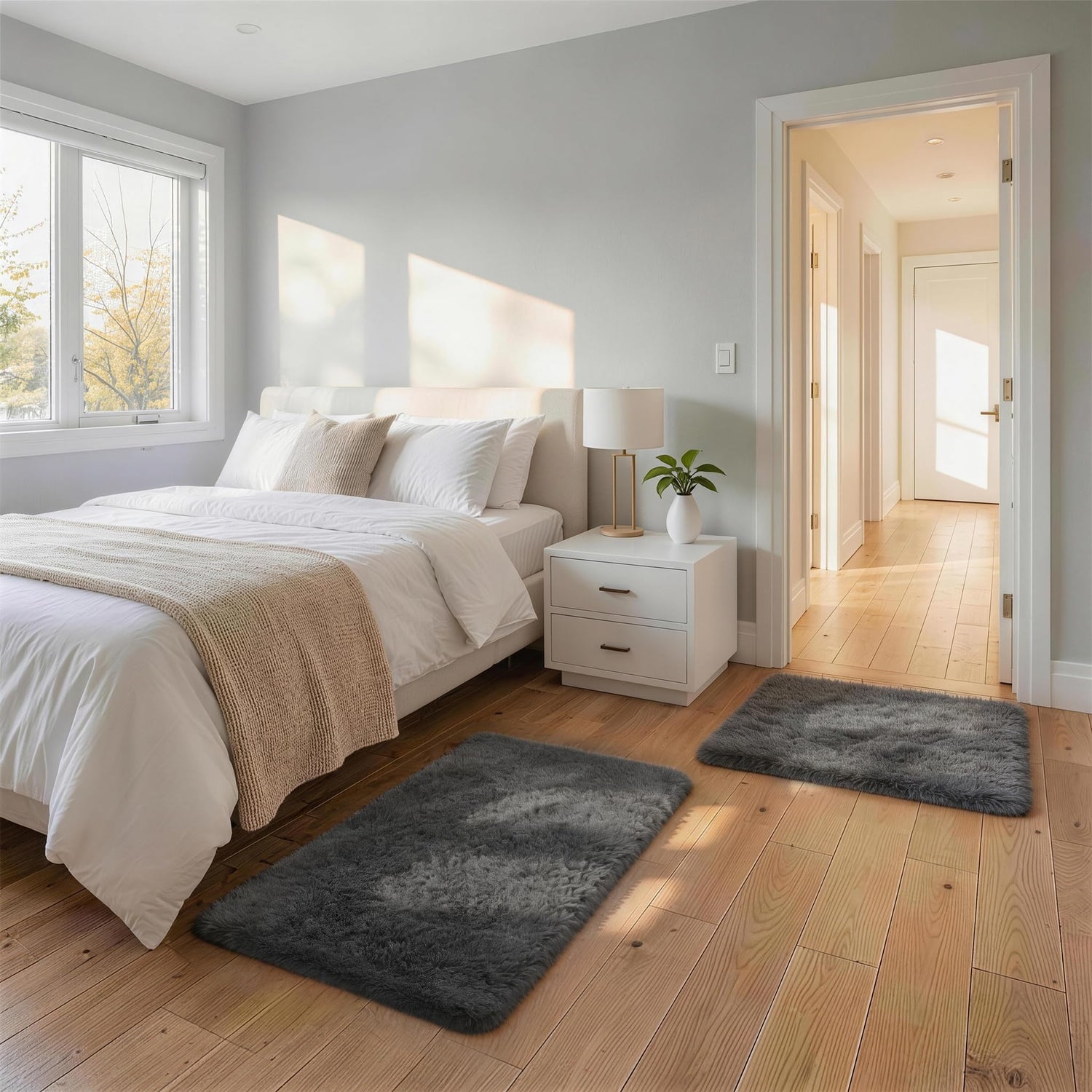 Bedroom scene with a white bed and two dark gray shag rugs on a light wood floor.