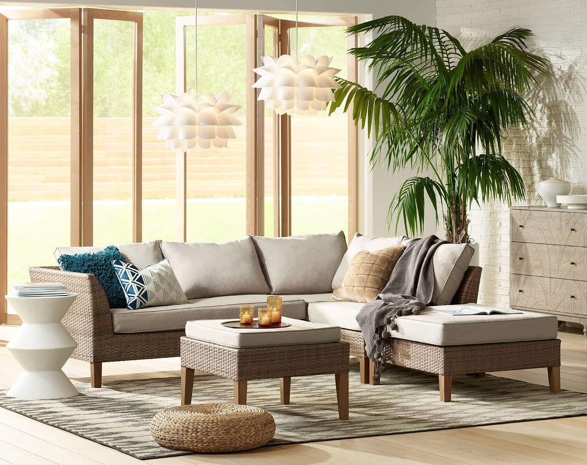 Two lit flower pendants hanging by a sunlit wall of wood-framed windows above a woven sectional and tall palm