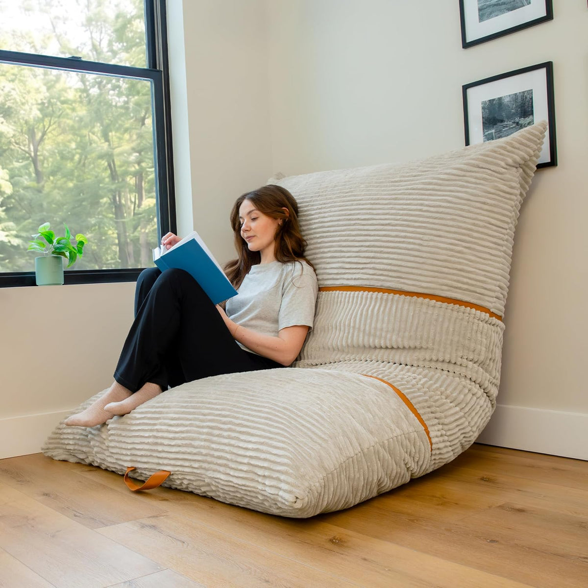 Woman reading while leaning back on a large cream corded lounge bean bag by a window