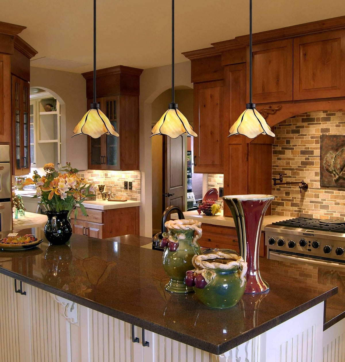Kitchen island scene showing three amber petal pendants hung over a dark polished countertop with decorative vases and