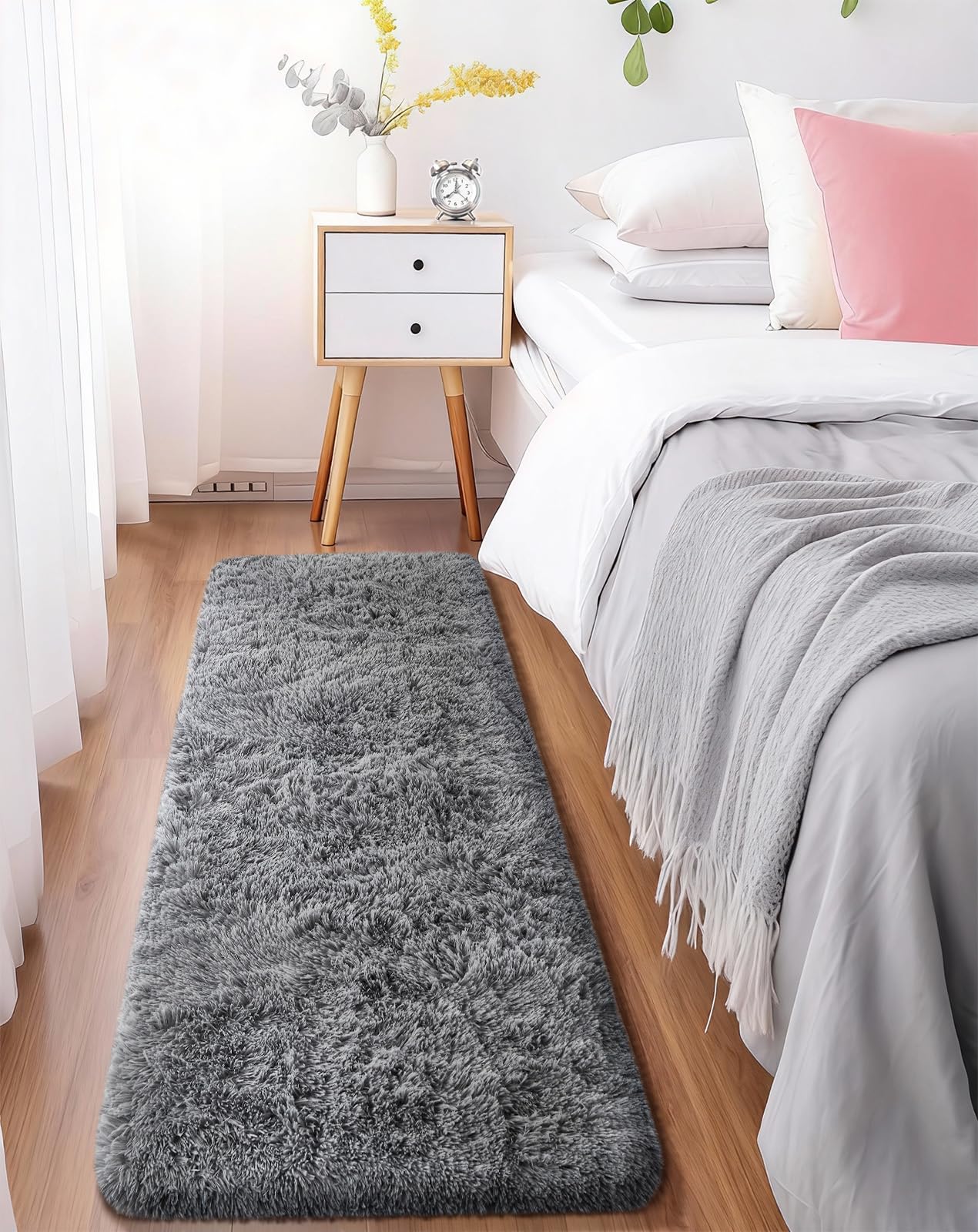 Long gray fluffy runner placed beside a bed with a white nightstand and soft bedding.
