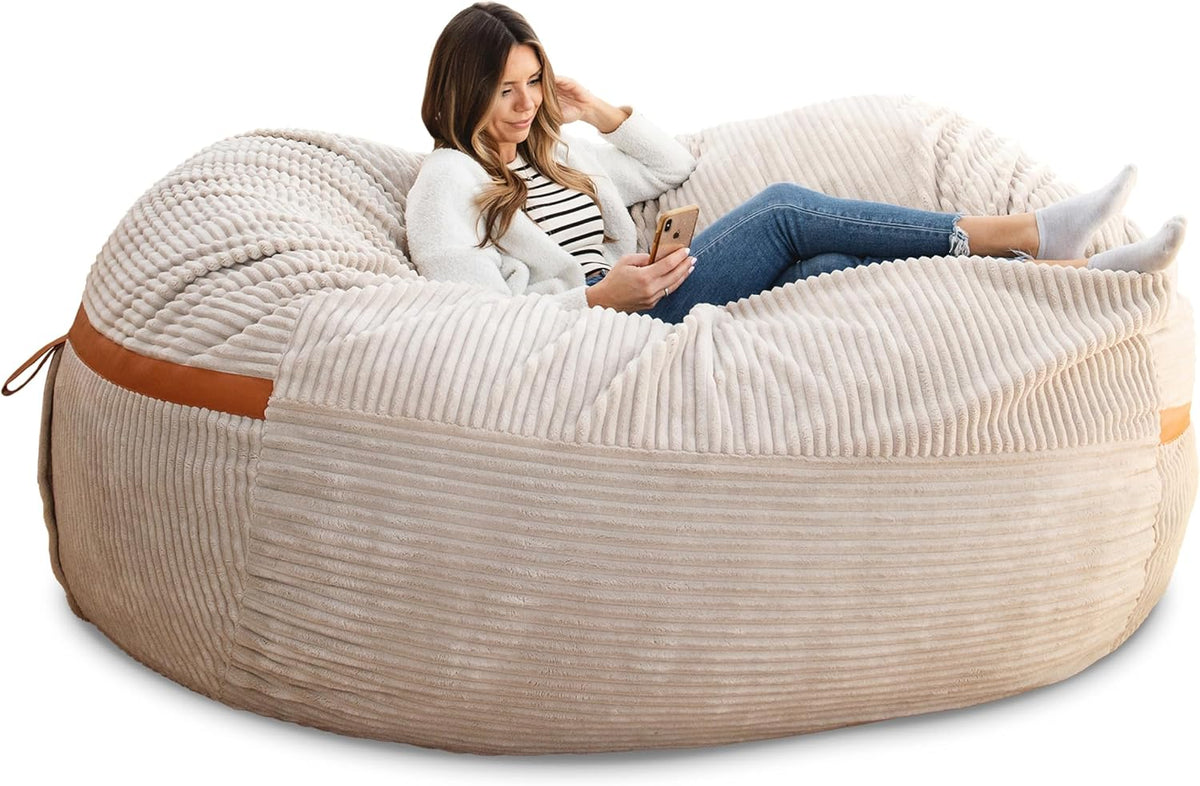 Side view of a woman reclining on a cream corded‑plush oversized lounger with tan trim and textured ribbing.