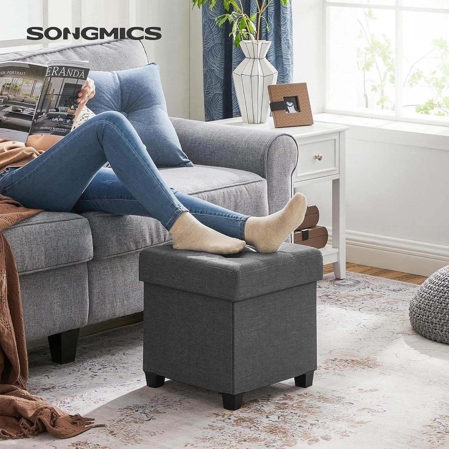 Dark gray ottoman used as a footrest in a living room setting beside a gray sofa