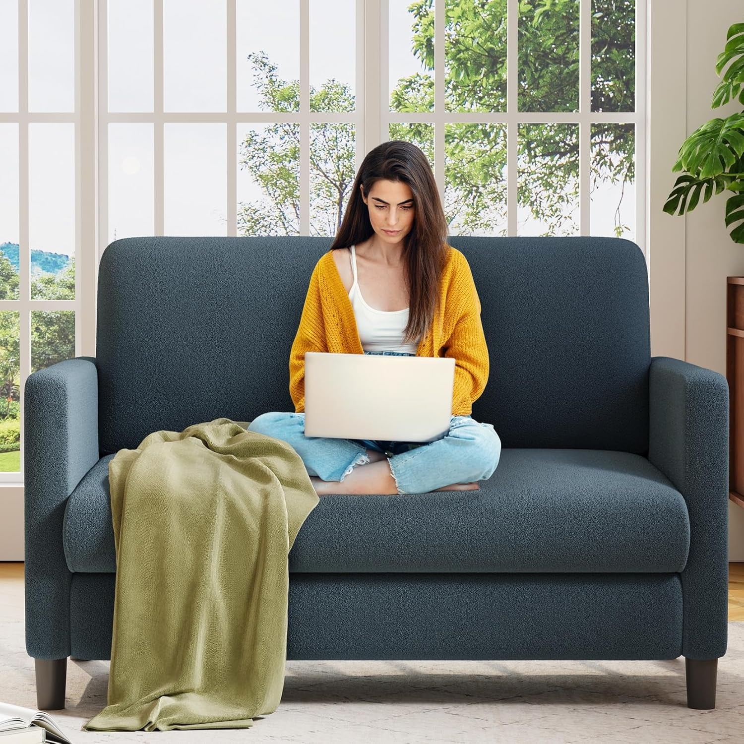 Grey Teddy fabric loveseat with a person sitting cross-legged using a laptop in front of a window