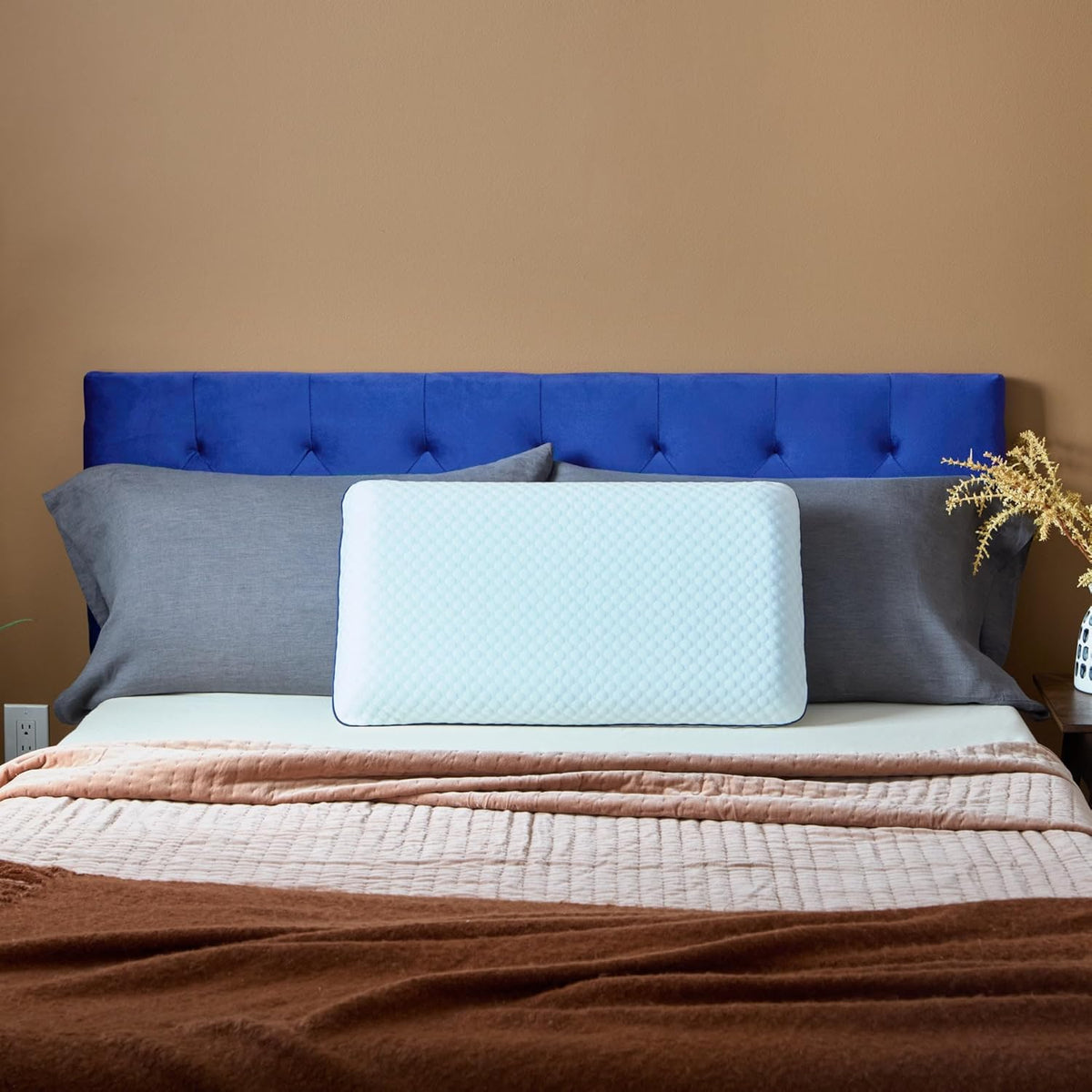 The pillow centred on a made bed with a blue tufted headboard and grey pillows
