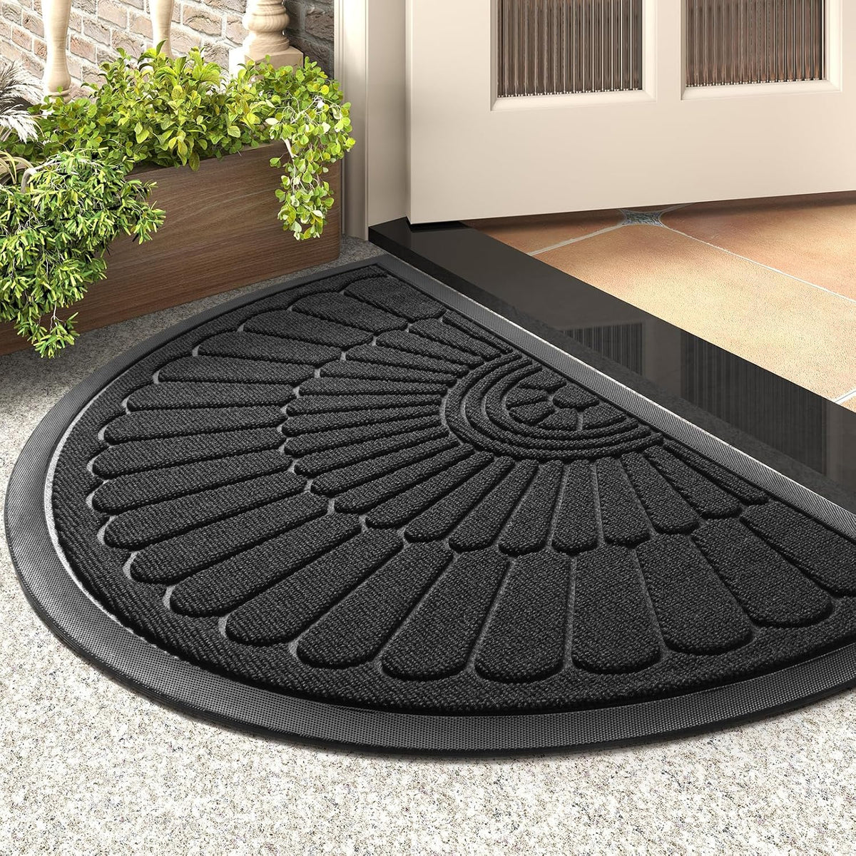 Close-up angled view of black semicircular doormat showing ribbed terry surface and beveled rubber edge on a stone floor