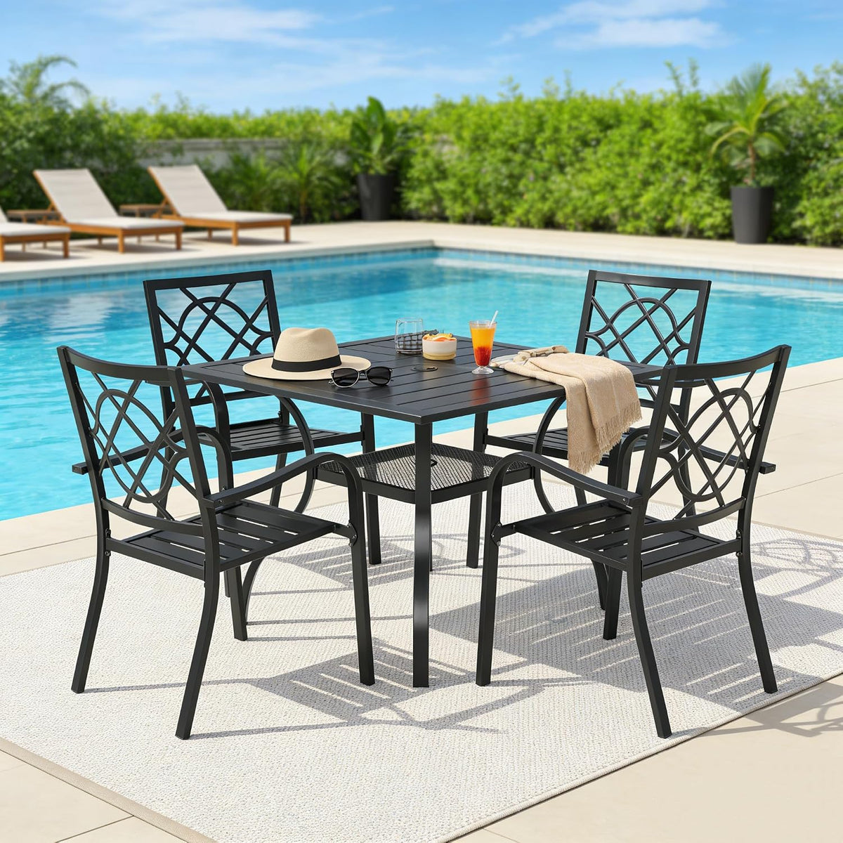 Black square table and four chairs beside a pool with tabletop accessories, front view
