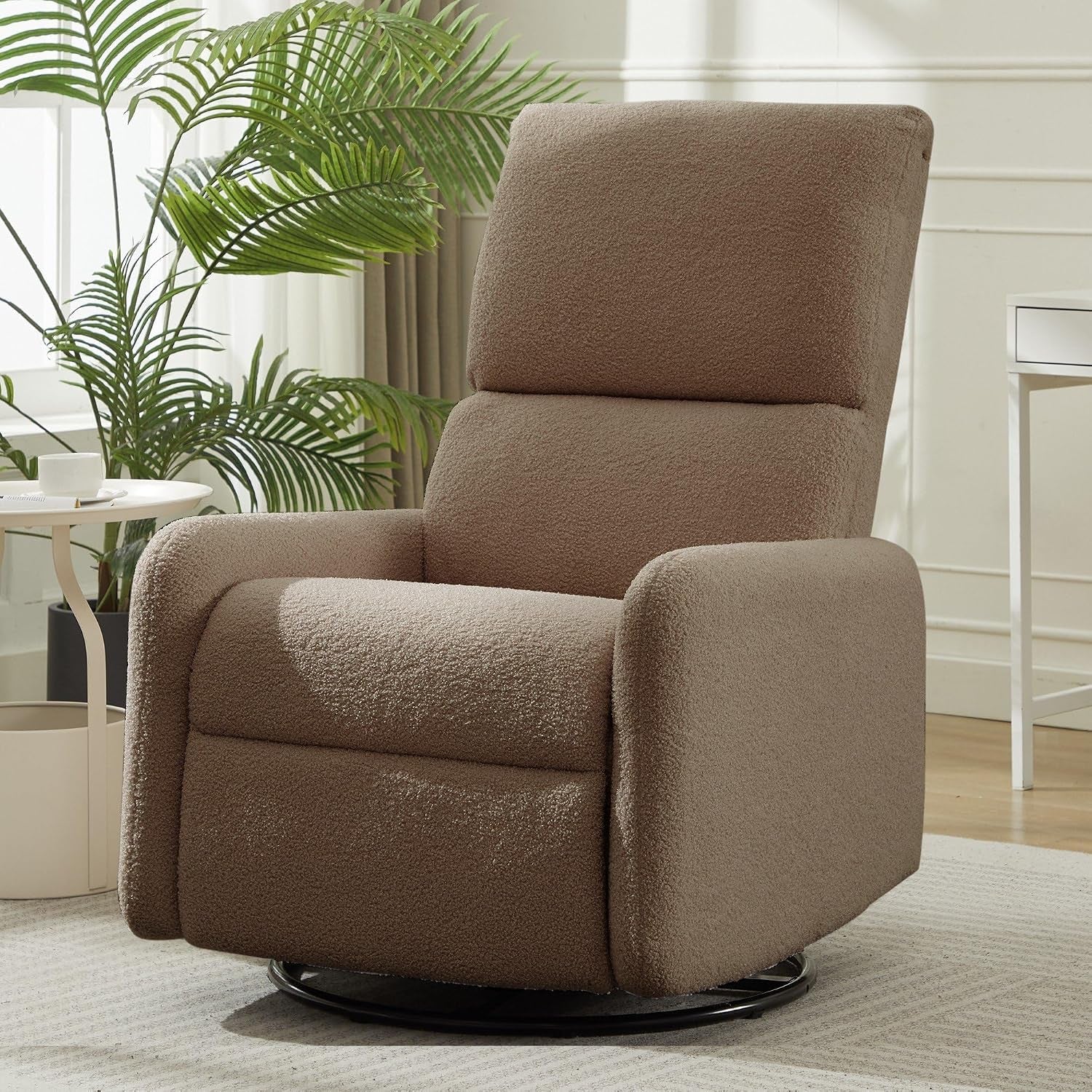Taupe sherpa swivel rocking chair in a sunny living room, shown angled with black circular base.