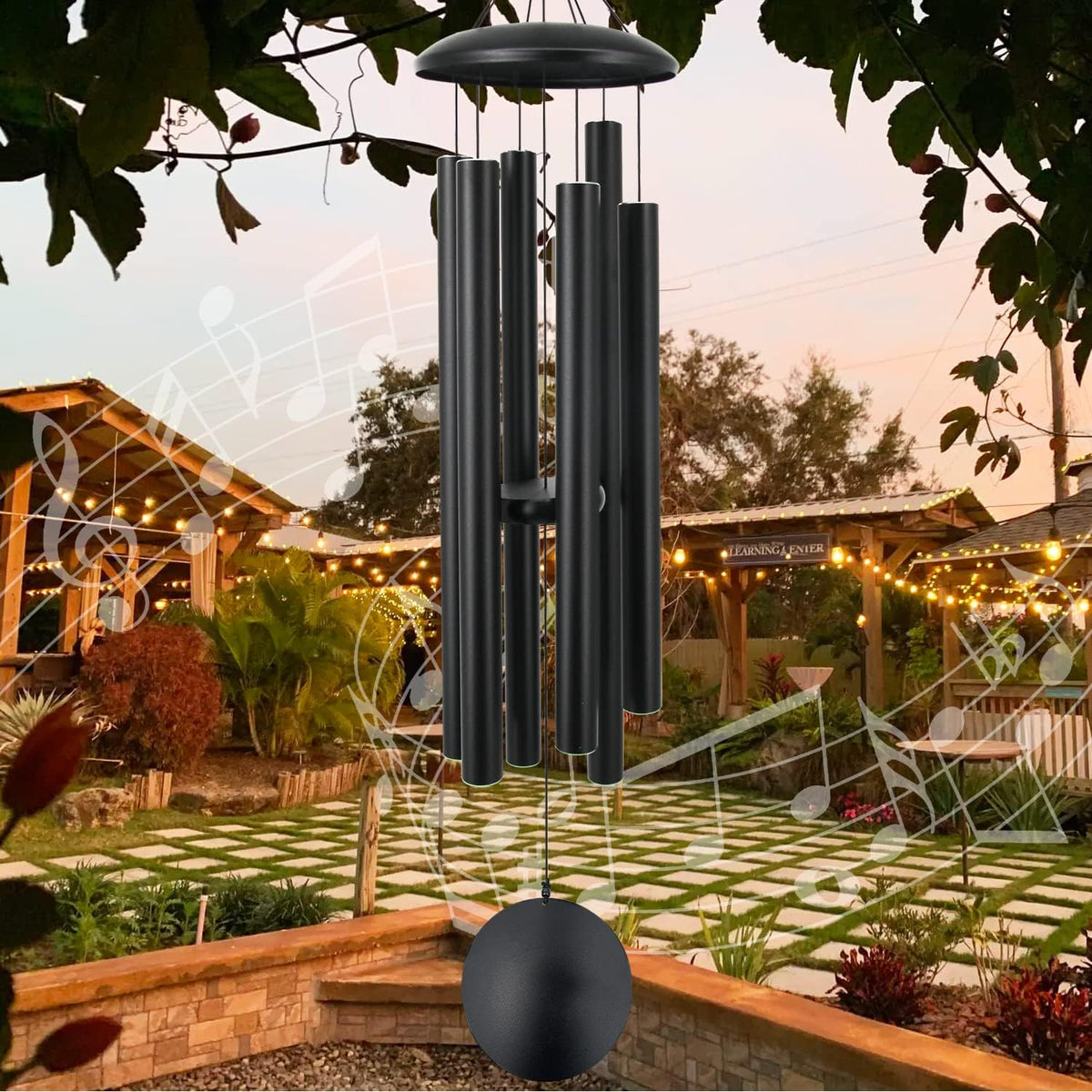 Black wind chime suspended outdoors at dusk with garden and string lights in background