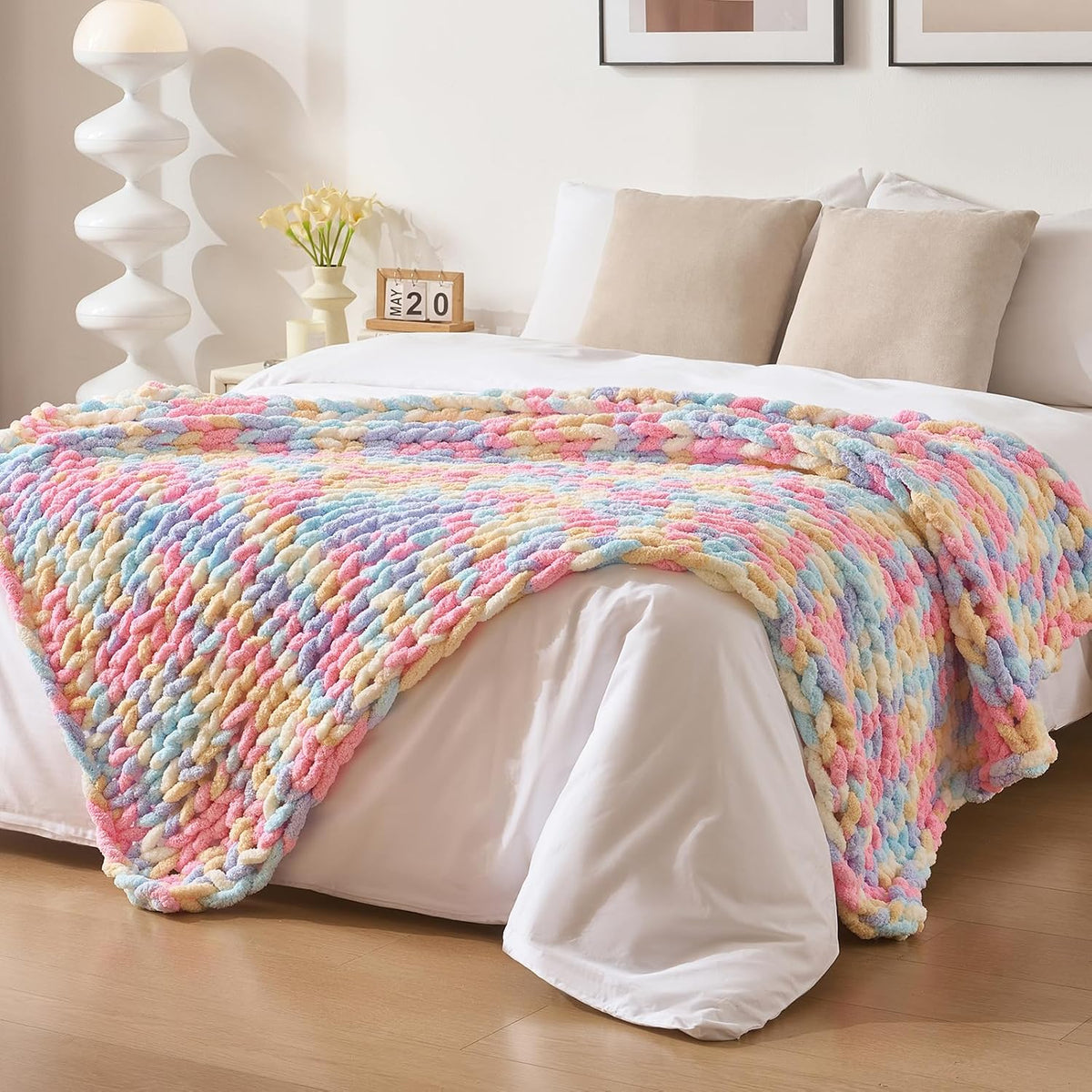 Pastel multicolor chunky knit throw spread across the foot of a white-made bed.