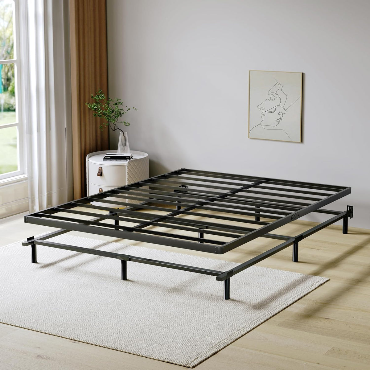 Low-profile black metal box spring installed on a bed frame in a bright bedroom, angled view