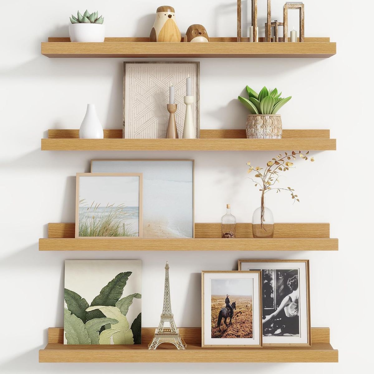 Four light-wood floating picture ledges stacked on a white wall holding framed art, a small Eiffel Tower and potted plants