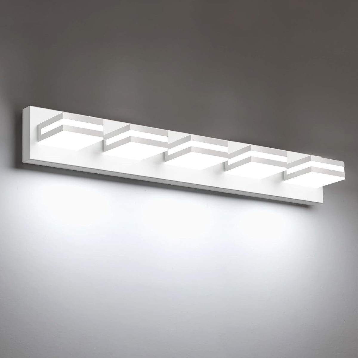 Angled view of a long four-light LED vanity fixture in matte white finish casting light on a pale wall.
