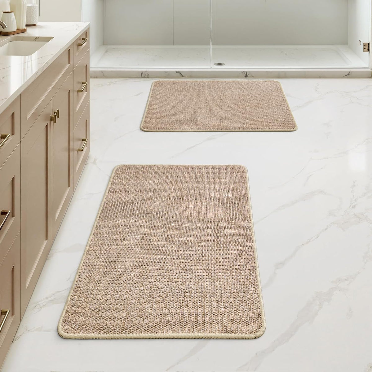 Bathroom floor with two rectangular beige rugs placed in front of shower and vanity.