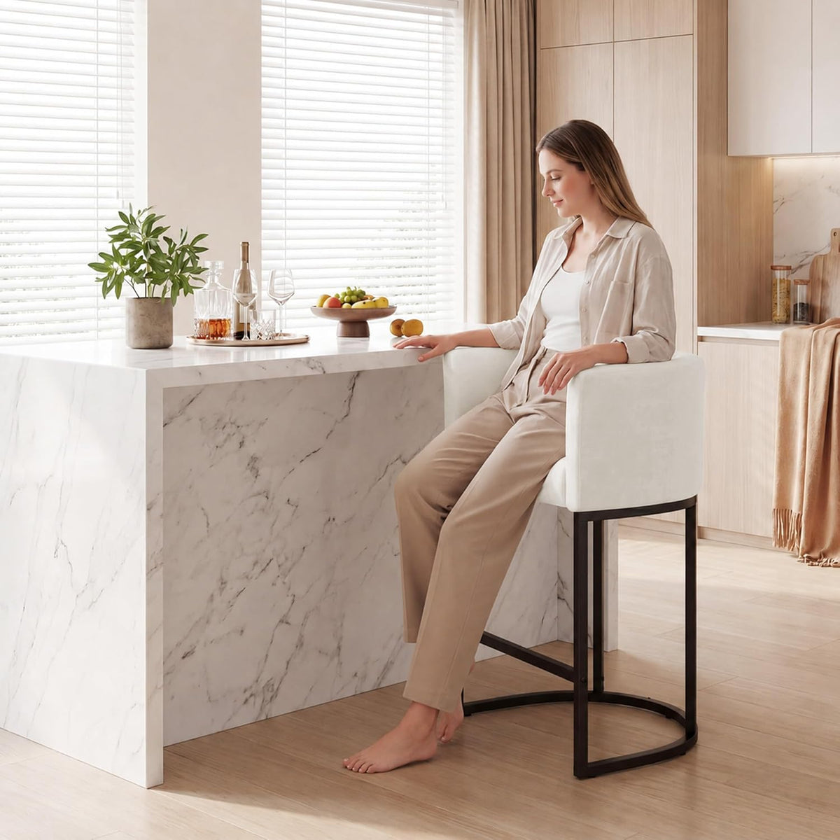 Woman seated on an off-white chenille counter stool at a marble counter demonstrating arm support and seating height