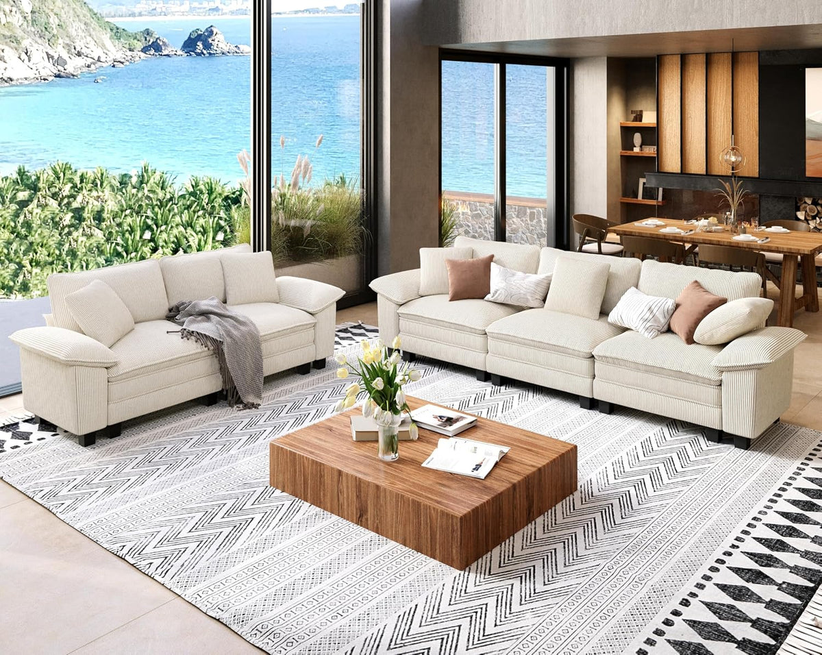 Bright living room with cream chenille three-seat sofa and loveseat on patterned rug by floor-to-ceiling windows.