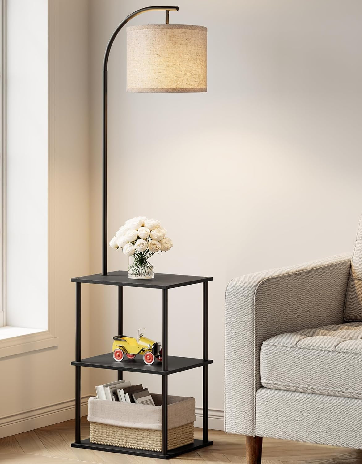 Arched floor lamp with drum shade built into a three-tier black side table holding a vase of white roses, toy car and woven