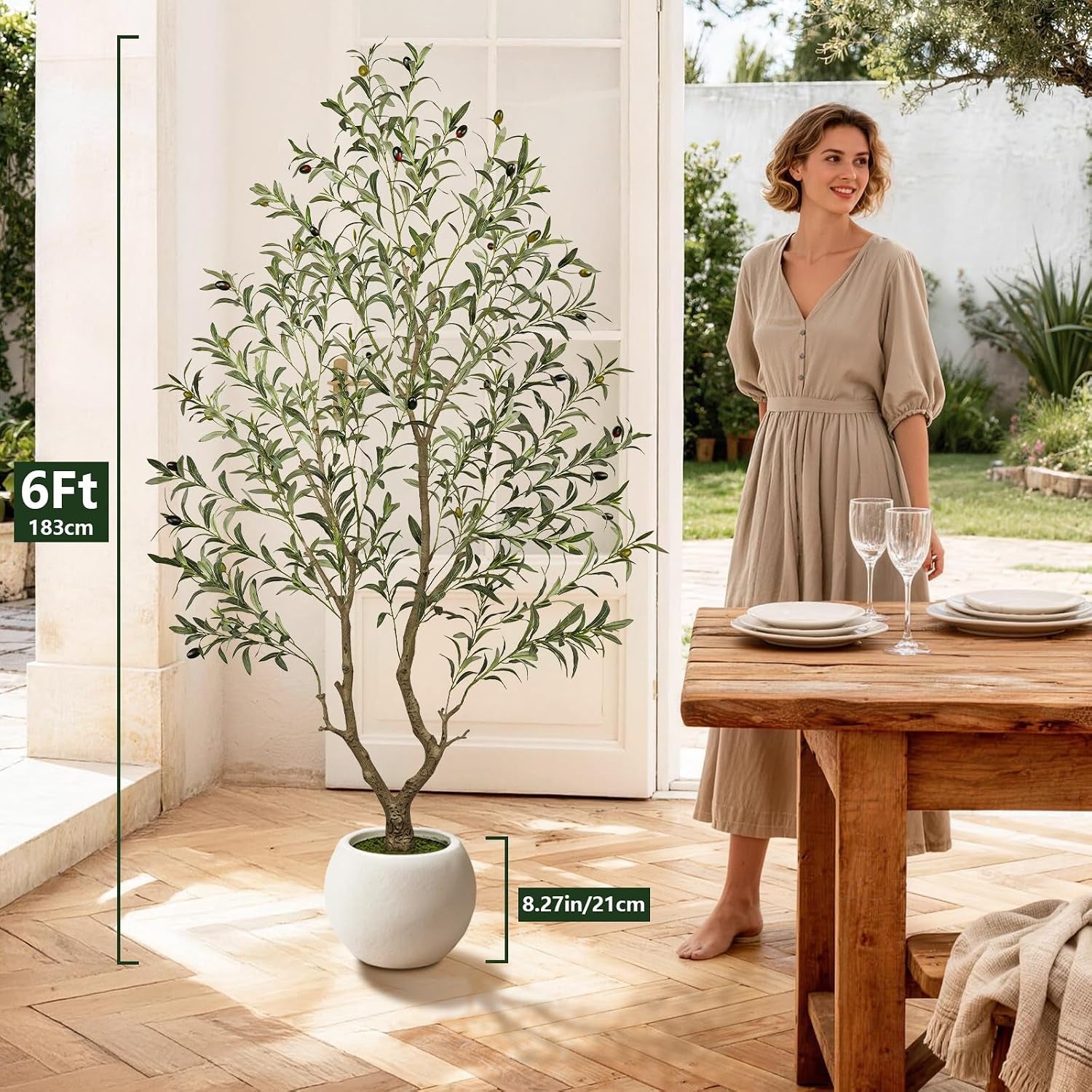 6ft artificial olive tree in a white round planter shown next to a doorway and dining table with a standing woman