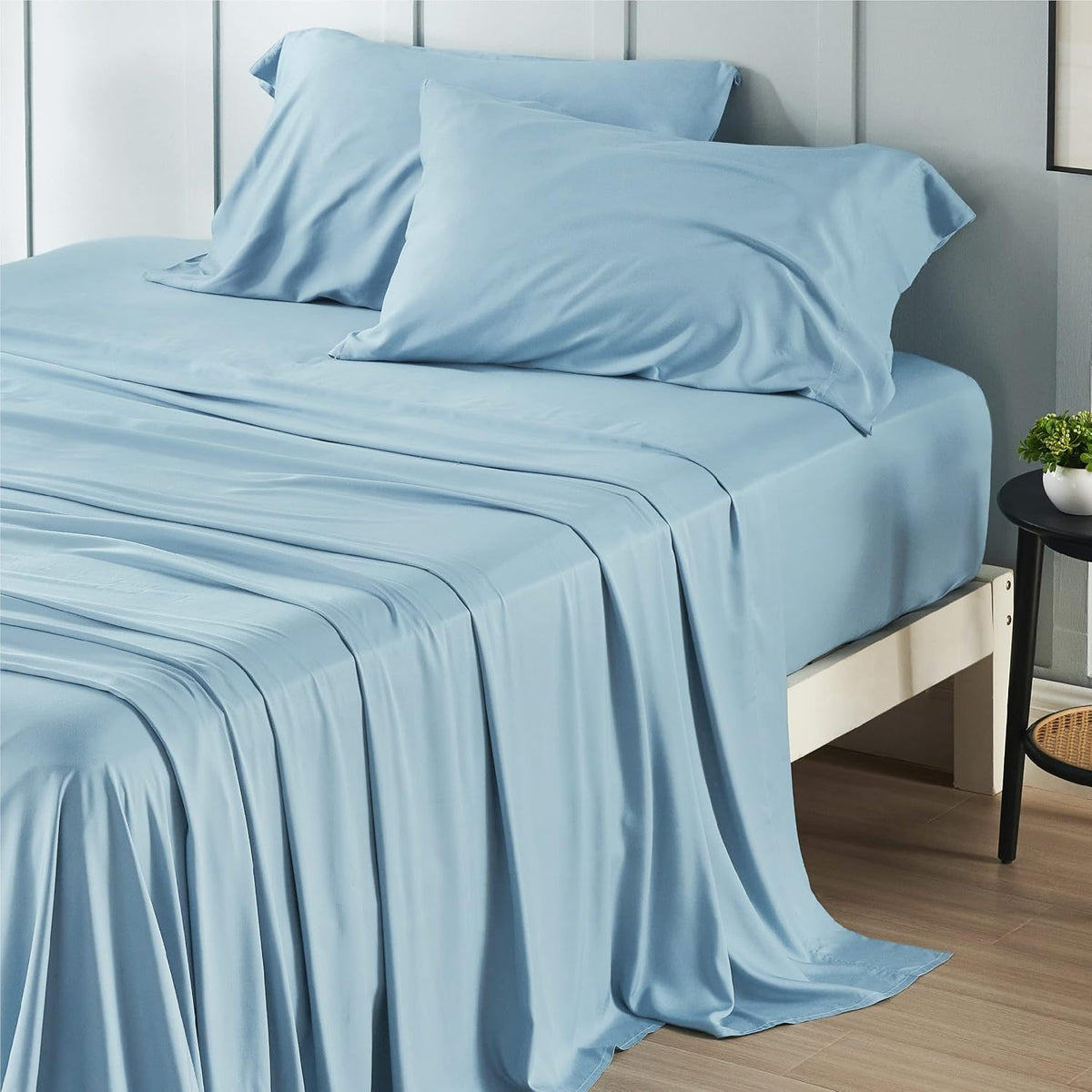 Close angled view of a bed with light blue silky sheets and two matching pillowcases draped over the mattress.