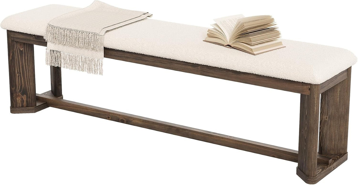 Studio side-angle of a long bench with white faux-lamb fur seat, fringed throw and open book on one end.