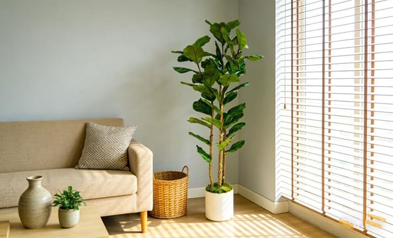 Artificial fiddle leaf fig in a white pot staged next to a neutral sofa and woven basket in a sunlit living room