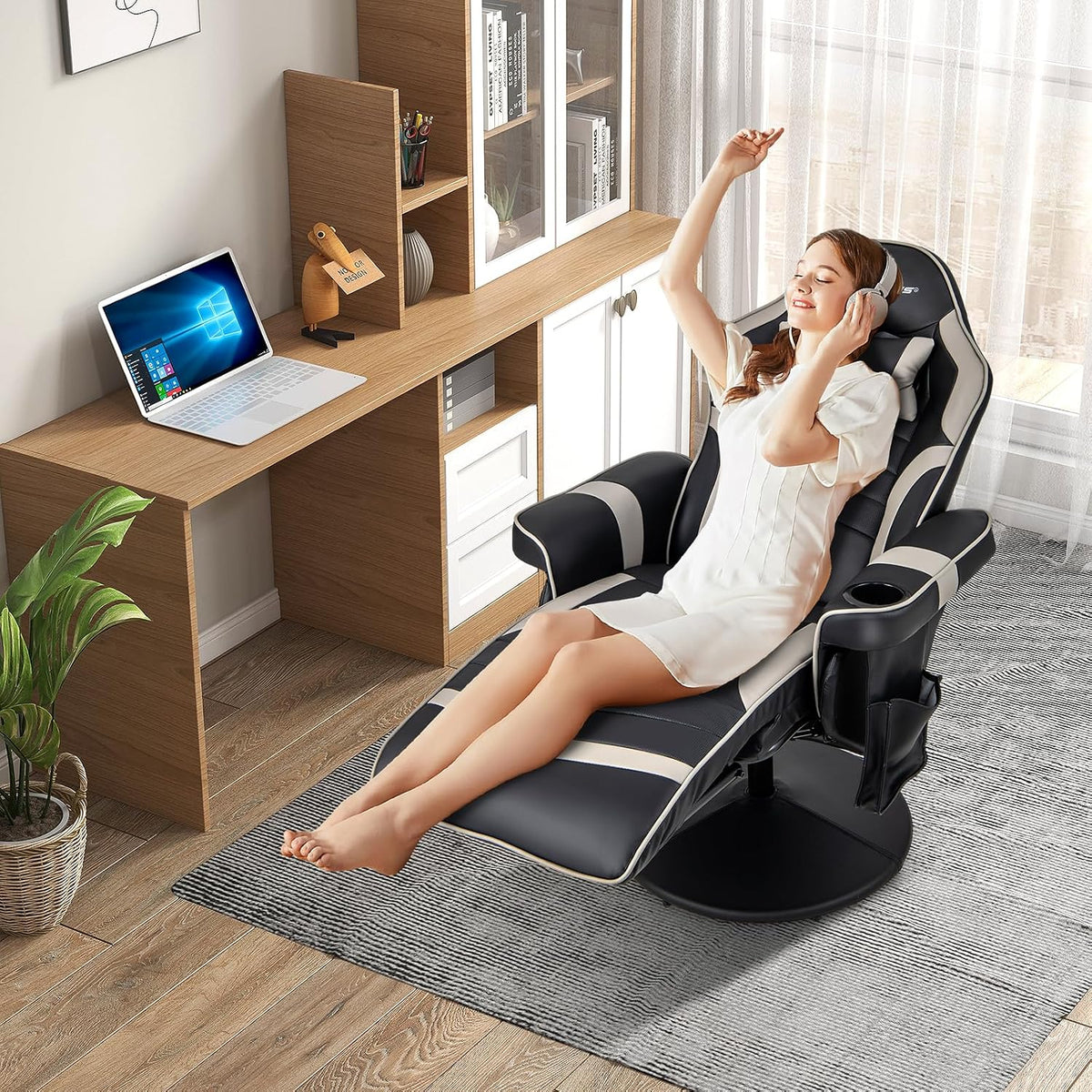Black and grey reclined gaming chair shown in a bright home office setting with a person relaxing