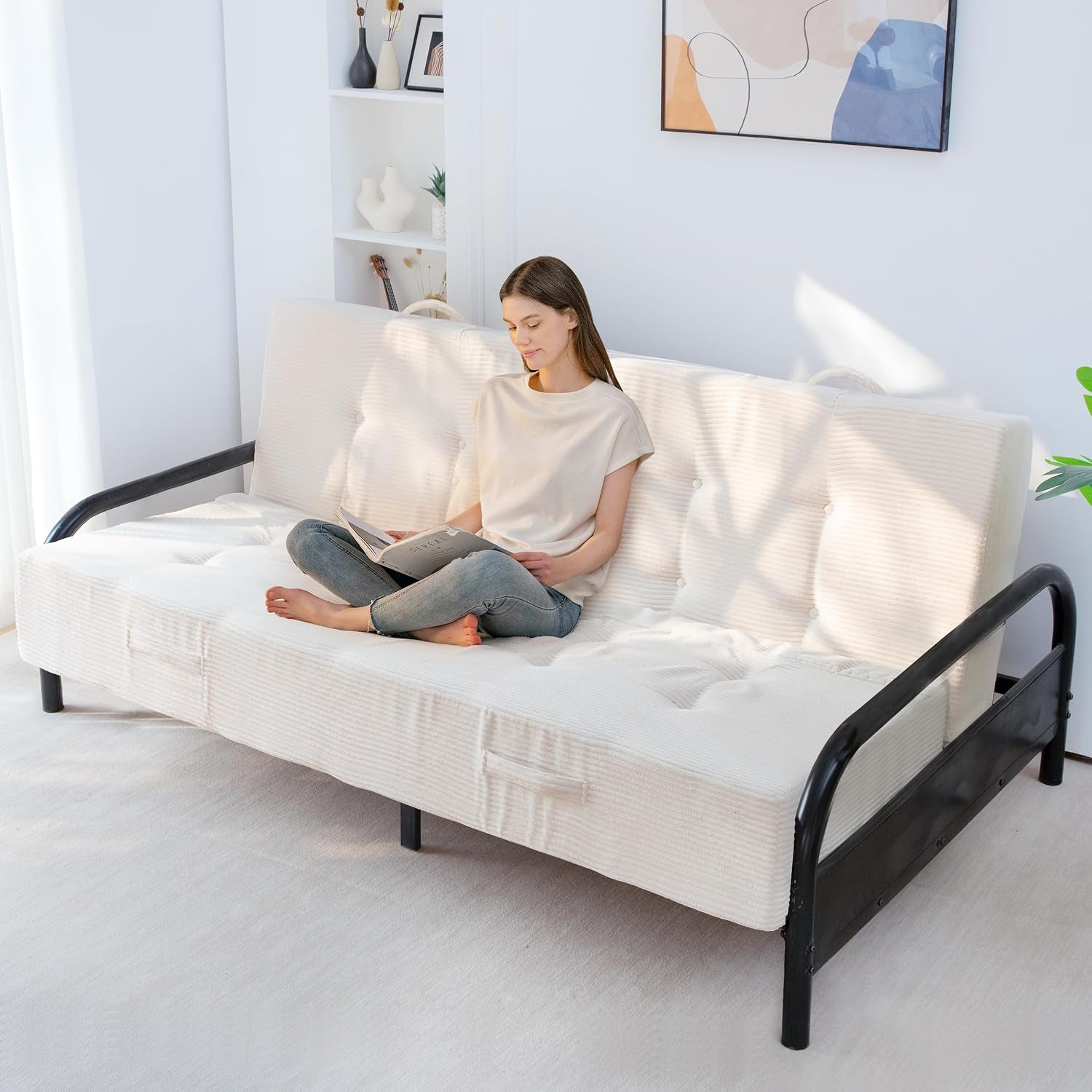 Woman seated cross-legged reading on a white corded futon mattress installed on a black metal frame.
