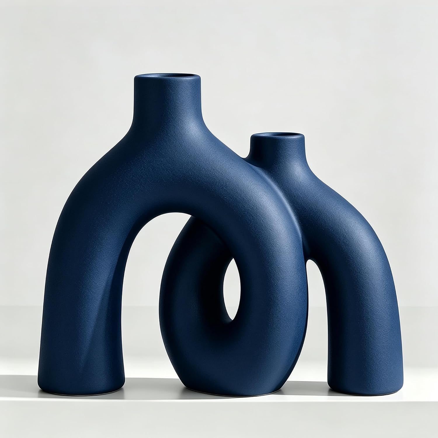 Same pair of sculptural donut ceramic vases in a deep matte navy blue, shown on a white surface.