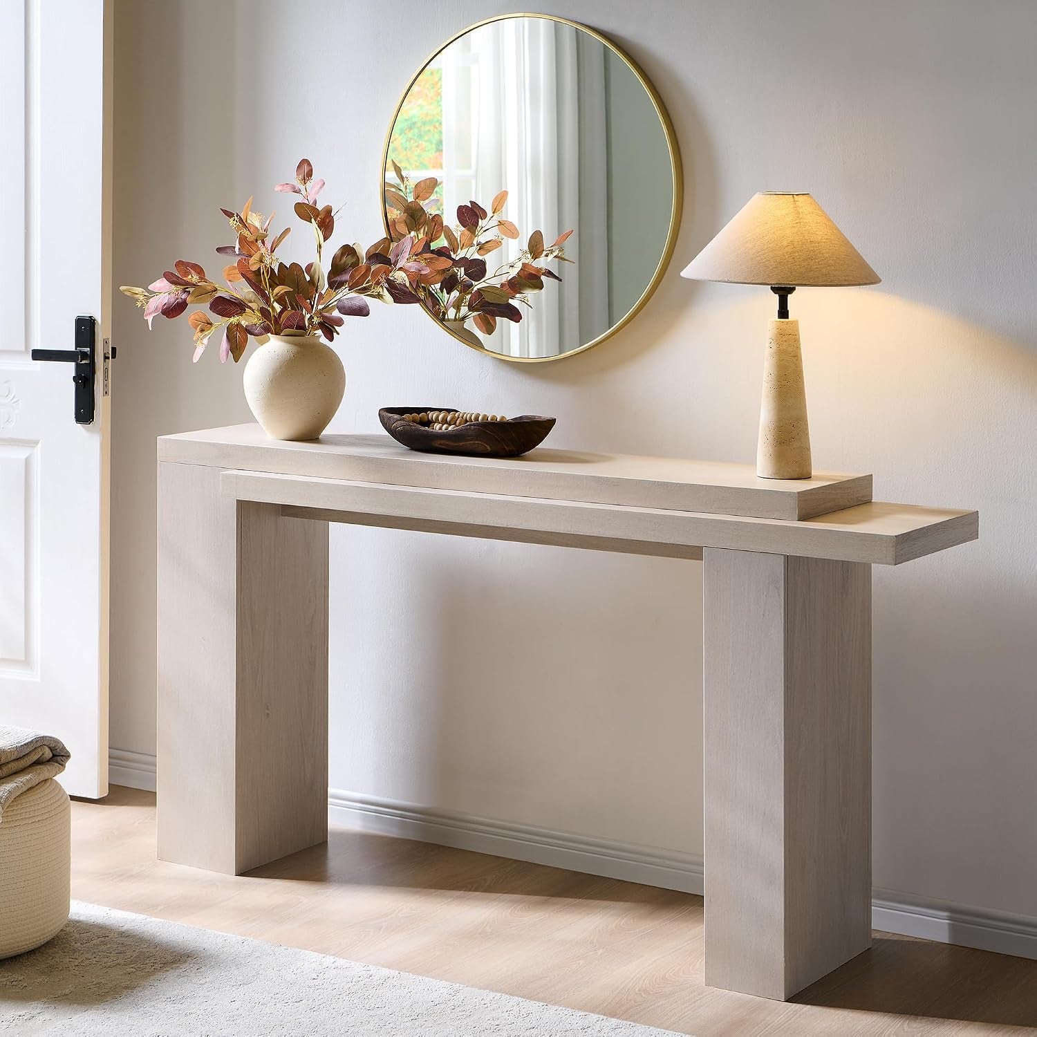 Side view of the layered console with a round gold-framed mirror, ceramic lamp and vase with foliage on the top tier.