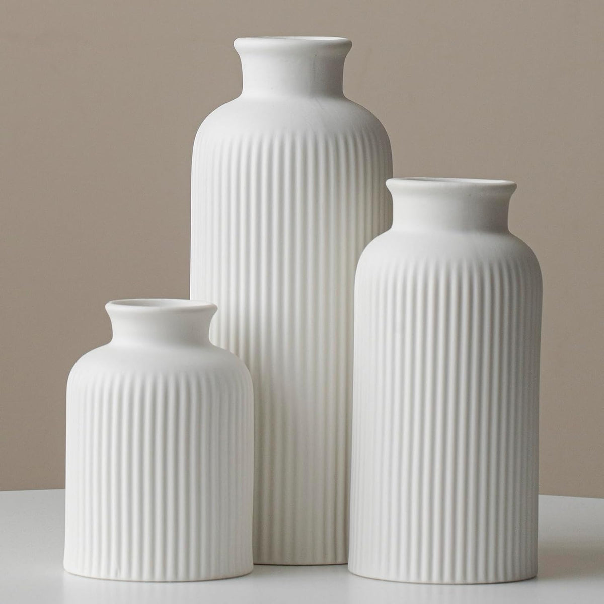 Three tall ribbed matte ceramic vases in off-white arranged close together on a white surface.