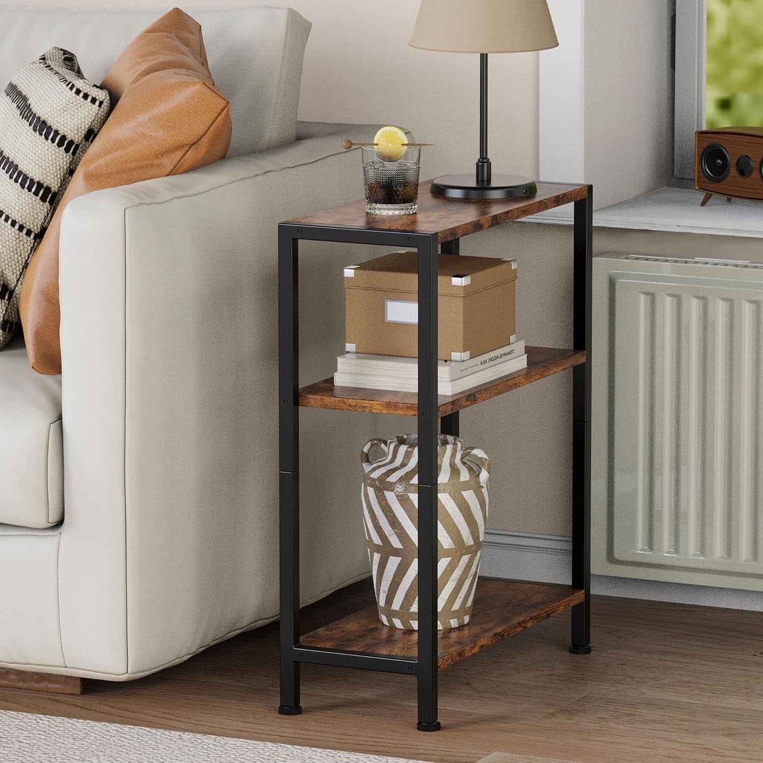 Narrow three-shelf side table beside a sofa styled with lamp and decor, side view in living room