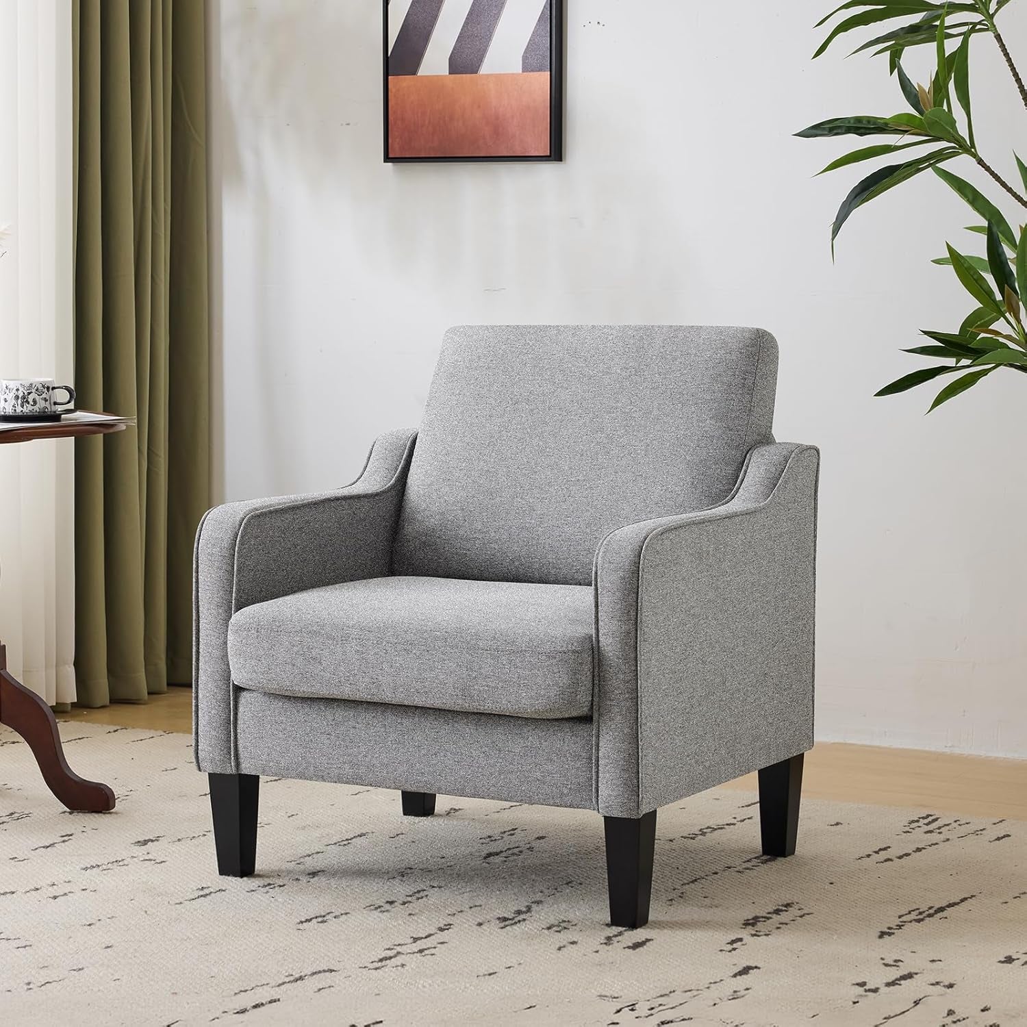 Light grey upholstered armchair on a patterned rug with curtains and wall art behind.
