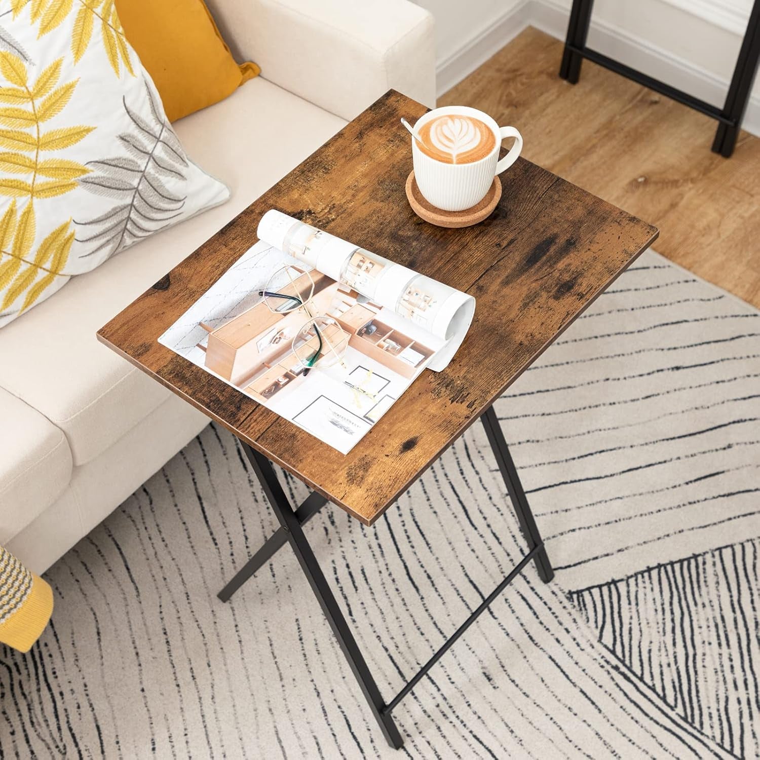 Rustic brown tray table next to a sofa holding a magazine and a cup, angled top-down view in a living room