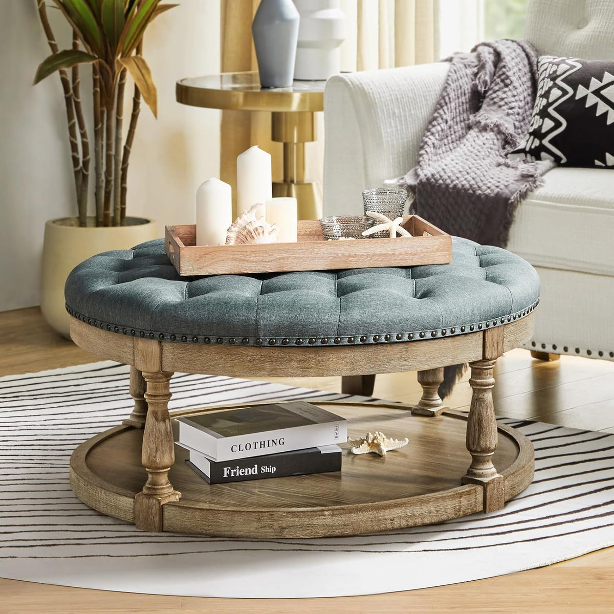Close-up living room view of round blue tufted ottoman used as a coffee table with a wooden tray and decor on top