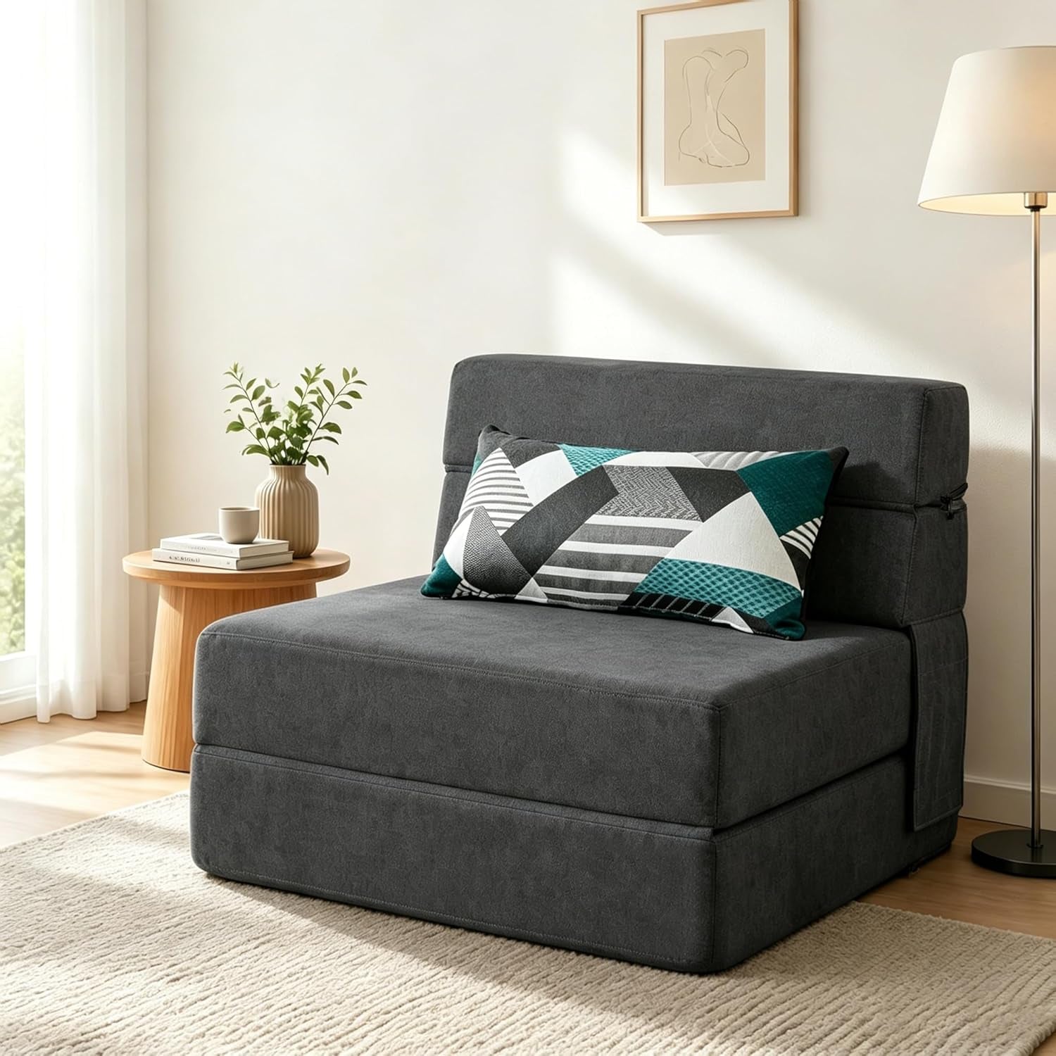 Dark gray folding futon chair with a geometric patterned pillow and nearby lamp