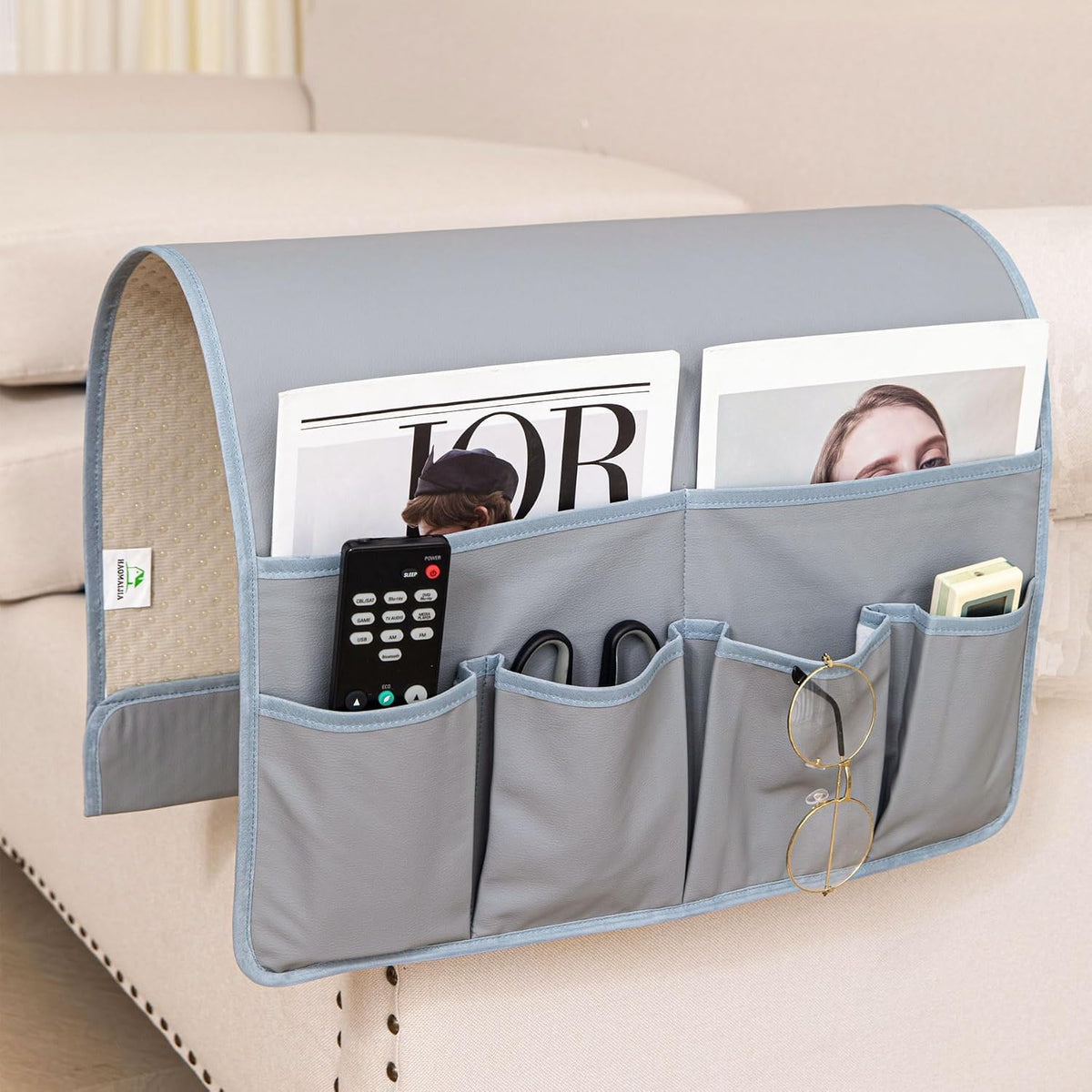 Light gray-blue armrest caddy hooked over a sofa arm holding remote, glasses and a small device.