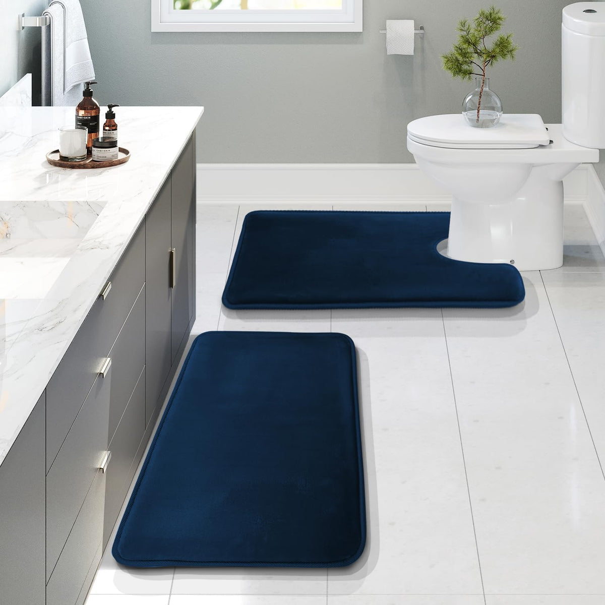 Bathroom scene with two navy blue bath mats placed by a vanity and a toilet on a tiled floor