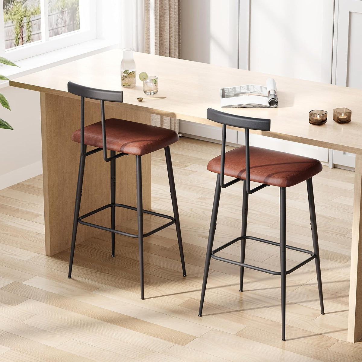 Pair of barstools with brown padded seats tucked under a light wood counter in a sunny kitchen.