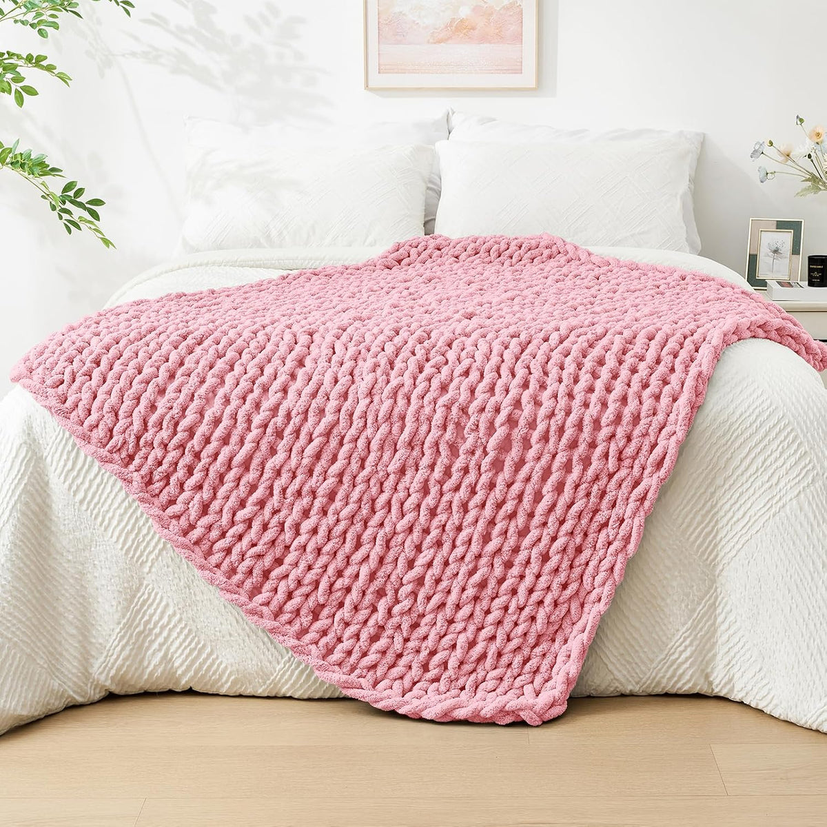 Soft pink chunky knit throw spread across the foot of a made bed with white pillows.