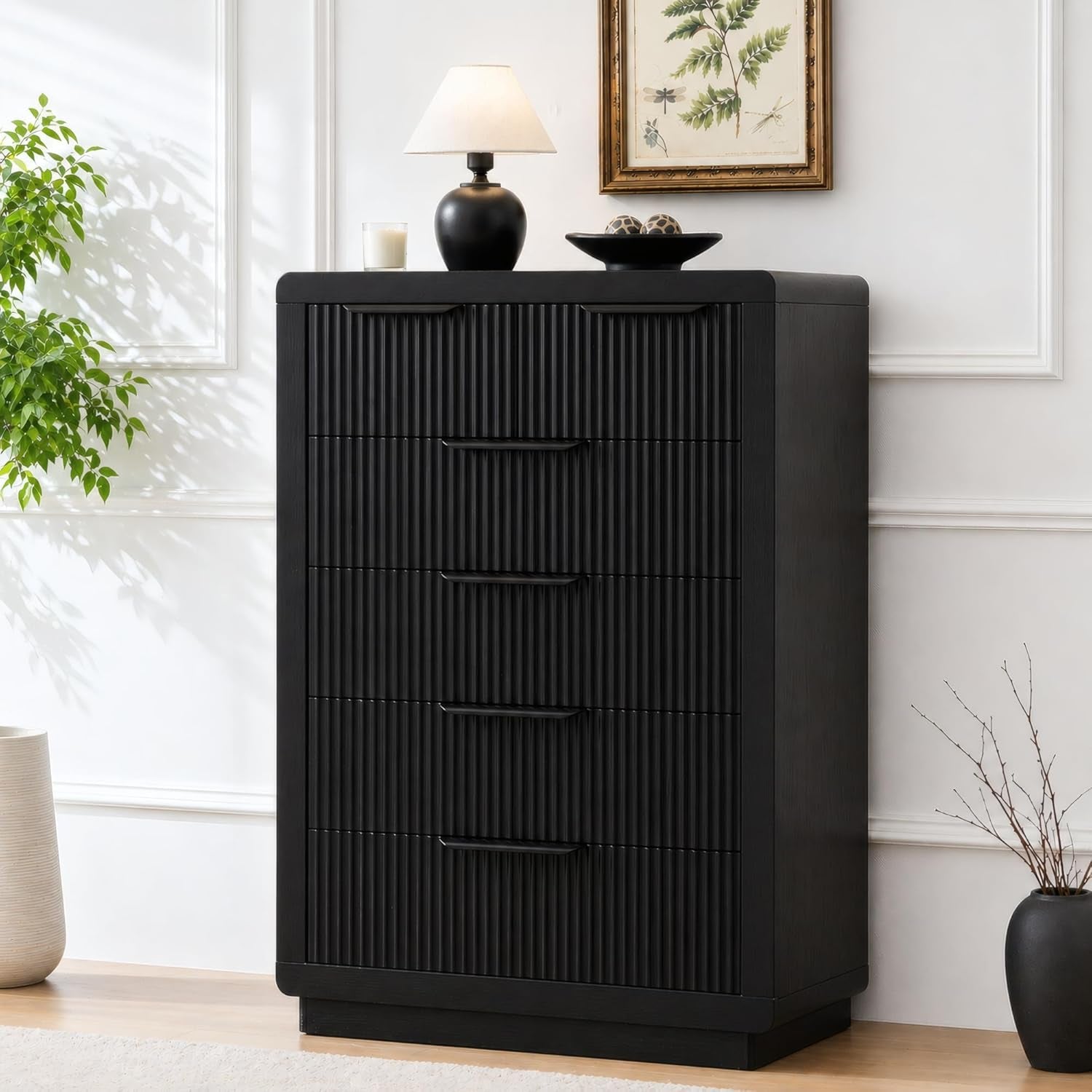 Tall black chest with vertically ribbed drawer fronts and slim black handles against a white wall.