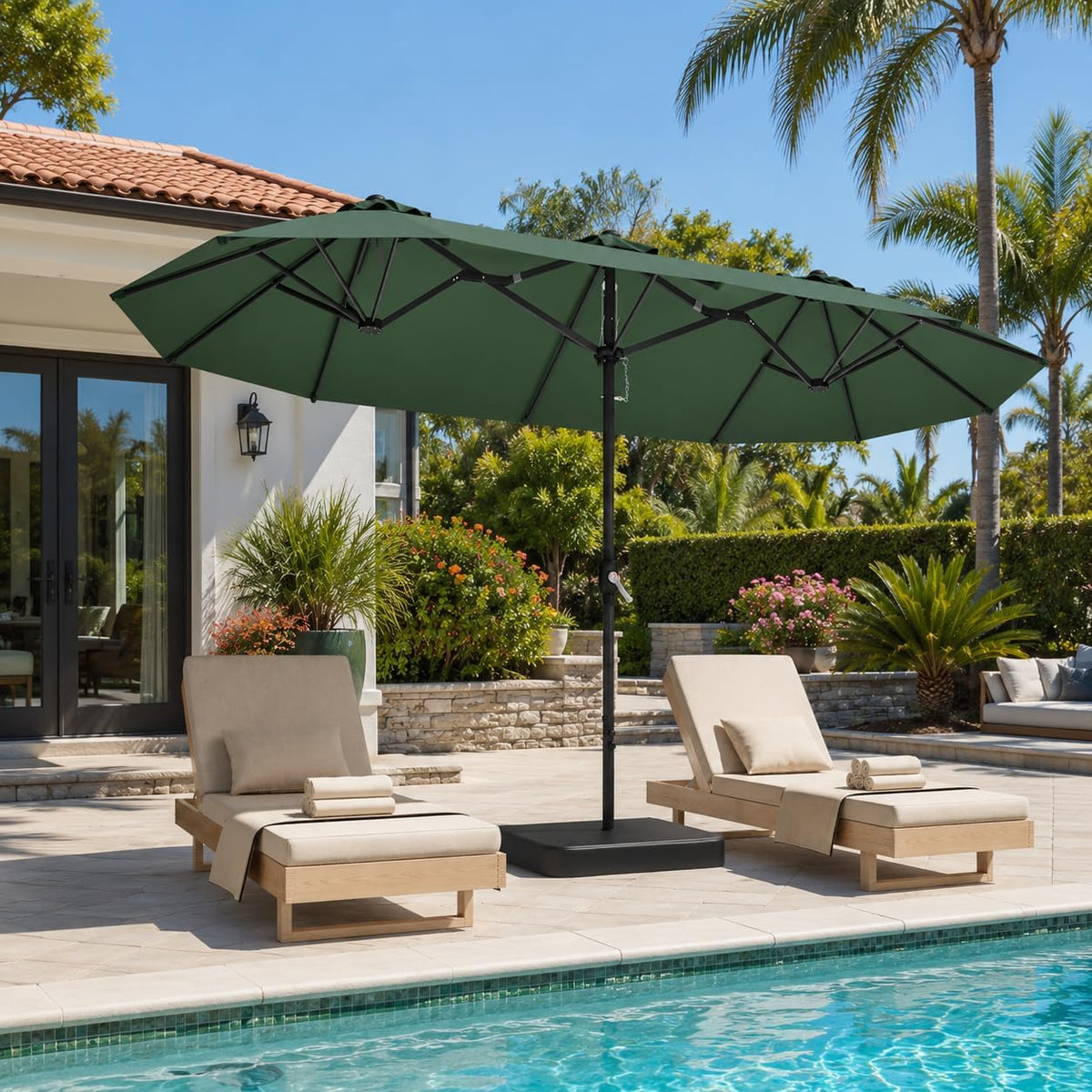 Green double-sided umbrella shading two beige chaise lounges next to a pool with palm trees.