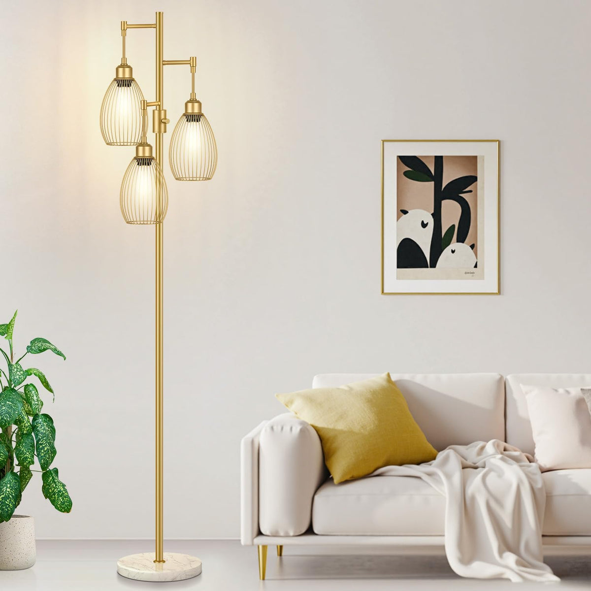 Gold floor lamp with three lit teardrop wire shades beside a white sofa and framed art